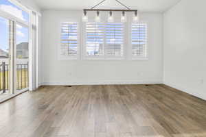 Spacious room featuring wood-finish flooring, white walls, and a modern linear chandelier