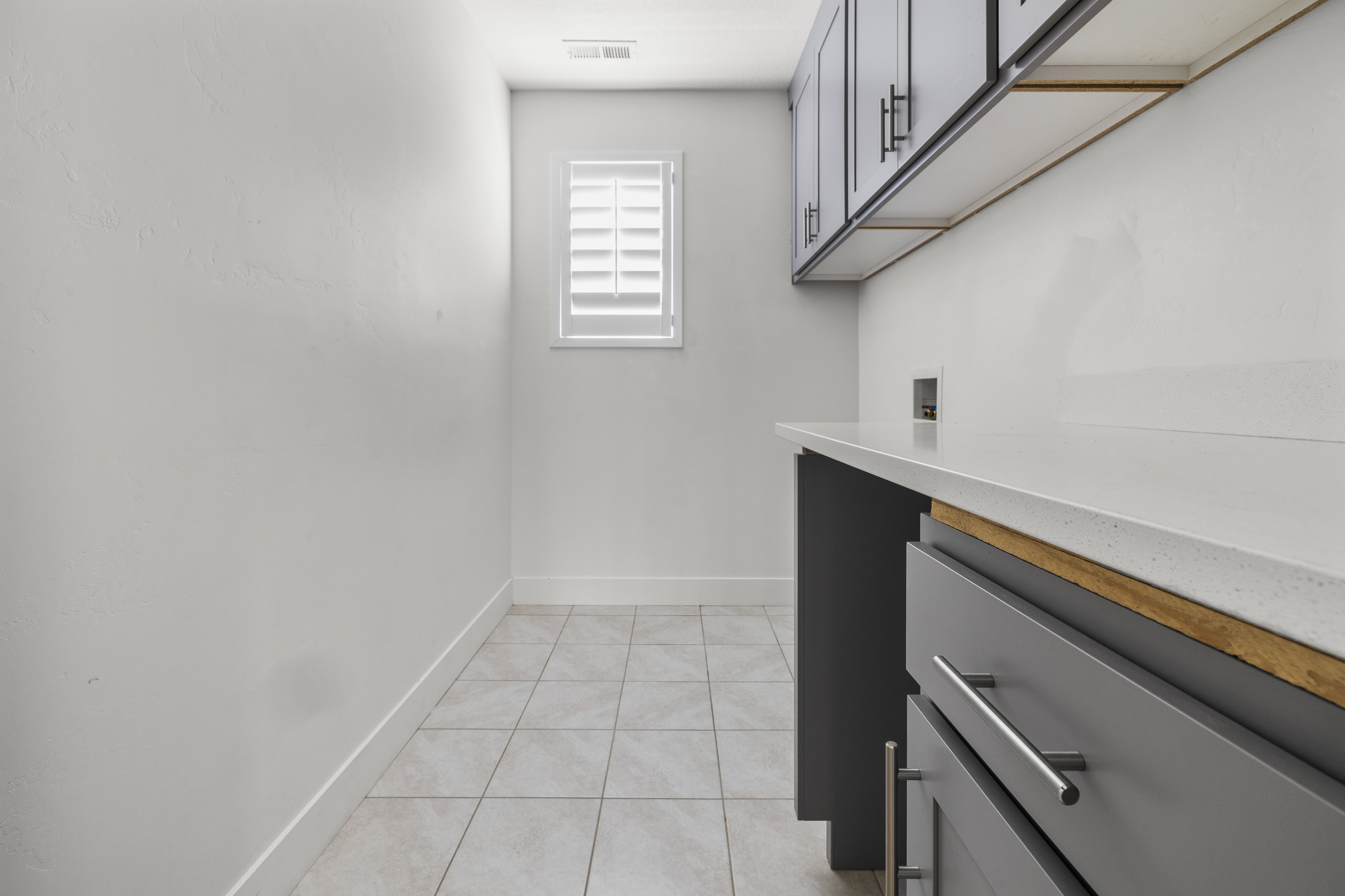 Laundry room featuring light grey tile flooring, white walls, and a window with white plantation shutters