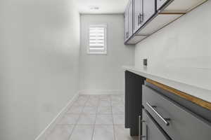 Laundry room featuring light grey tile flooring, white walls, and a window with white plantation shutters