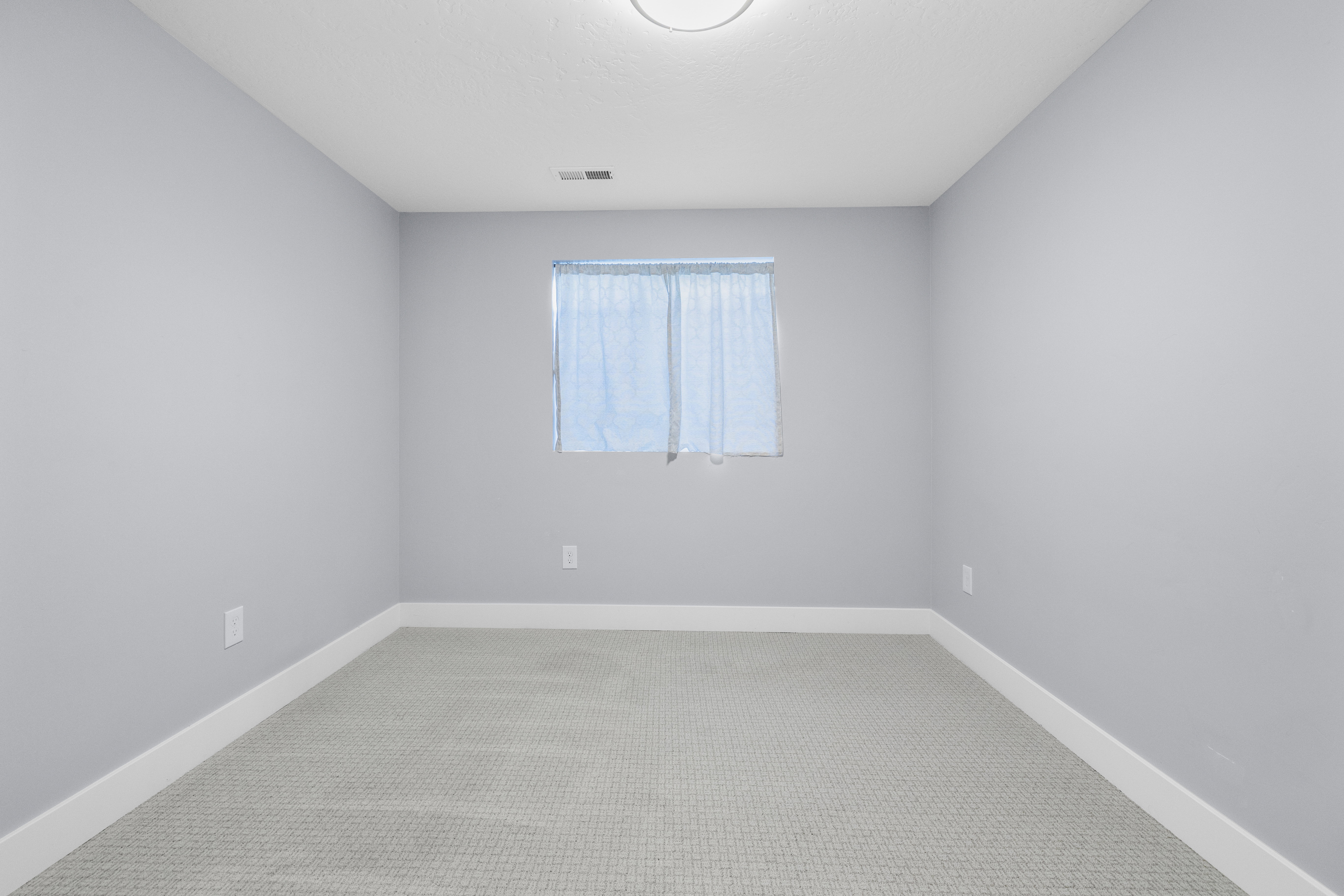 Spacious bedroom featuring neutral paint, light gray patterned carpeting, a single window, and a flush-mount ceiling light