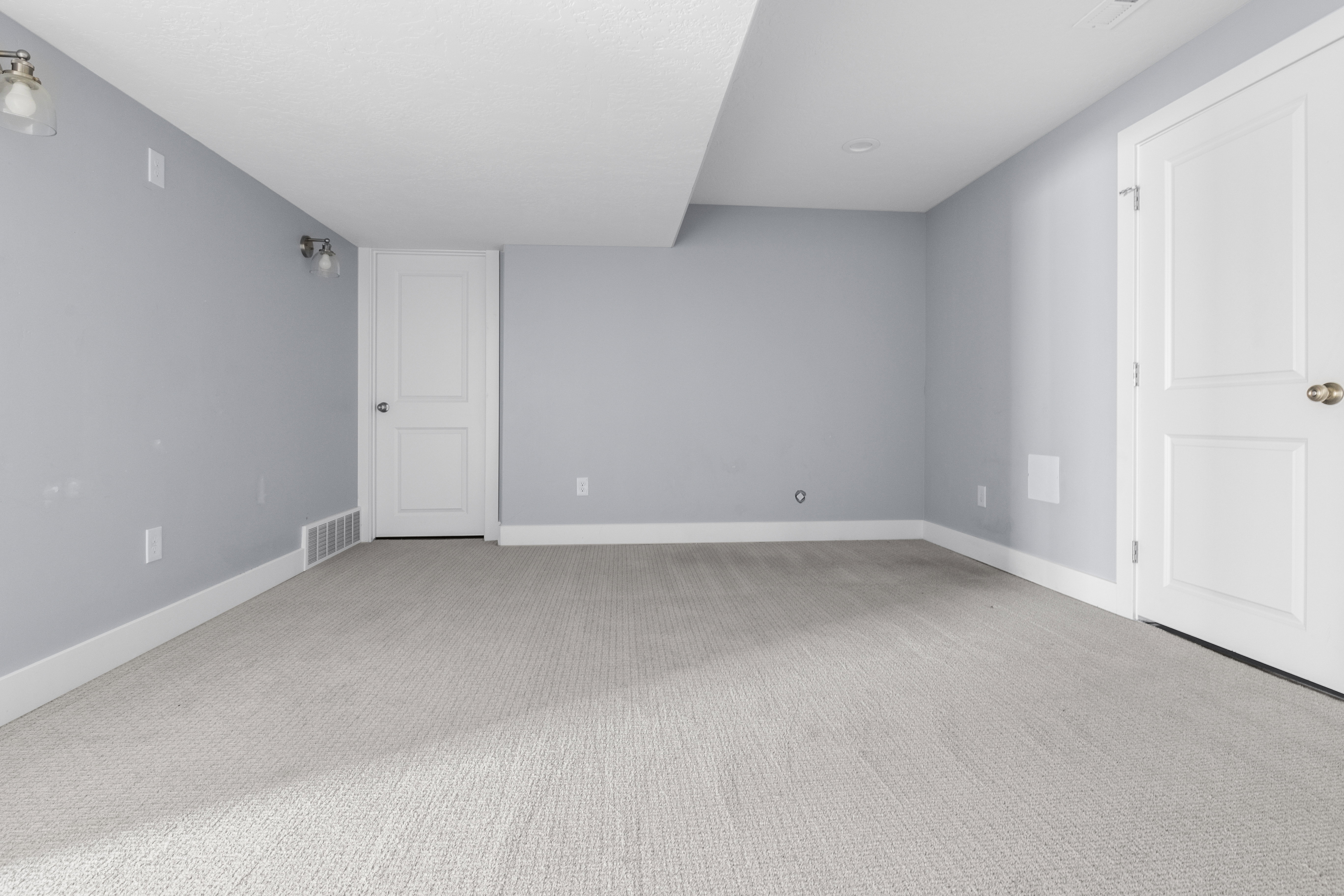 Spacious room with light gray carpeting, neutral wall paint, white trim, and two white paneled doors