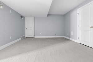 Spacious room with light gray carpeting, neutral wall paint, white trim, and two white paneled doors