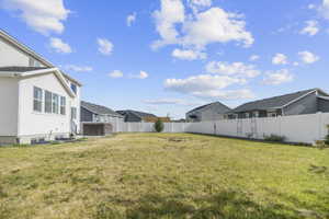 Spacious rear yard featuring a privacy fence, mature landscaping, and a side patio with an included spa