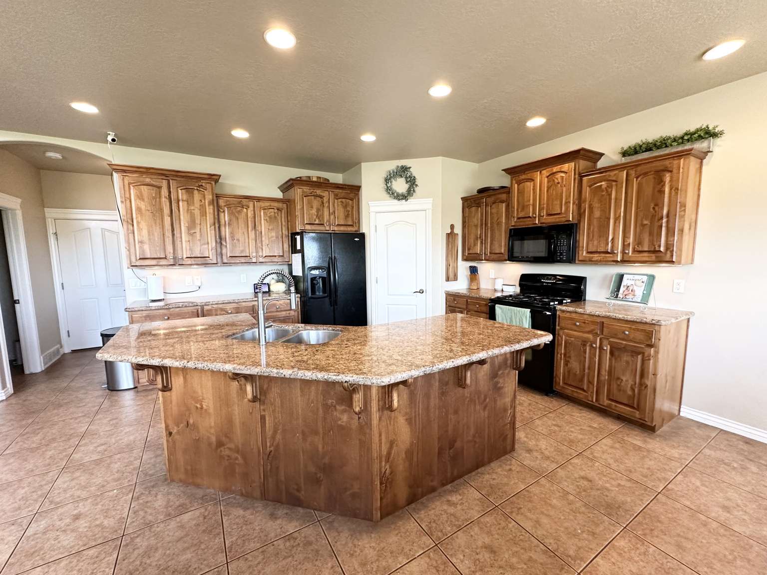 Kitchen featuring a central island with dual sinks and granite countertops, abundant wood cabinetry, black appliances including a range and refrigerator, and recessed lighting