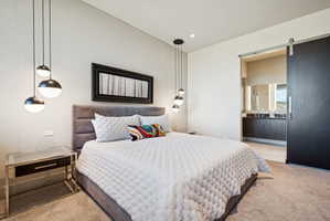 Bedroom with a barn door, light colored carpet, ensuite bath, and recessed lighting