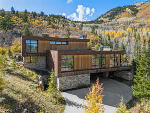 View of front facade featuring stone siding, a mountain view, a view of trees, and a carport