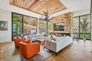 Living area with floor to ceiling windows, a wood tray ceiling, light wood-type flooring, plenty of natural light, and a chandelier