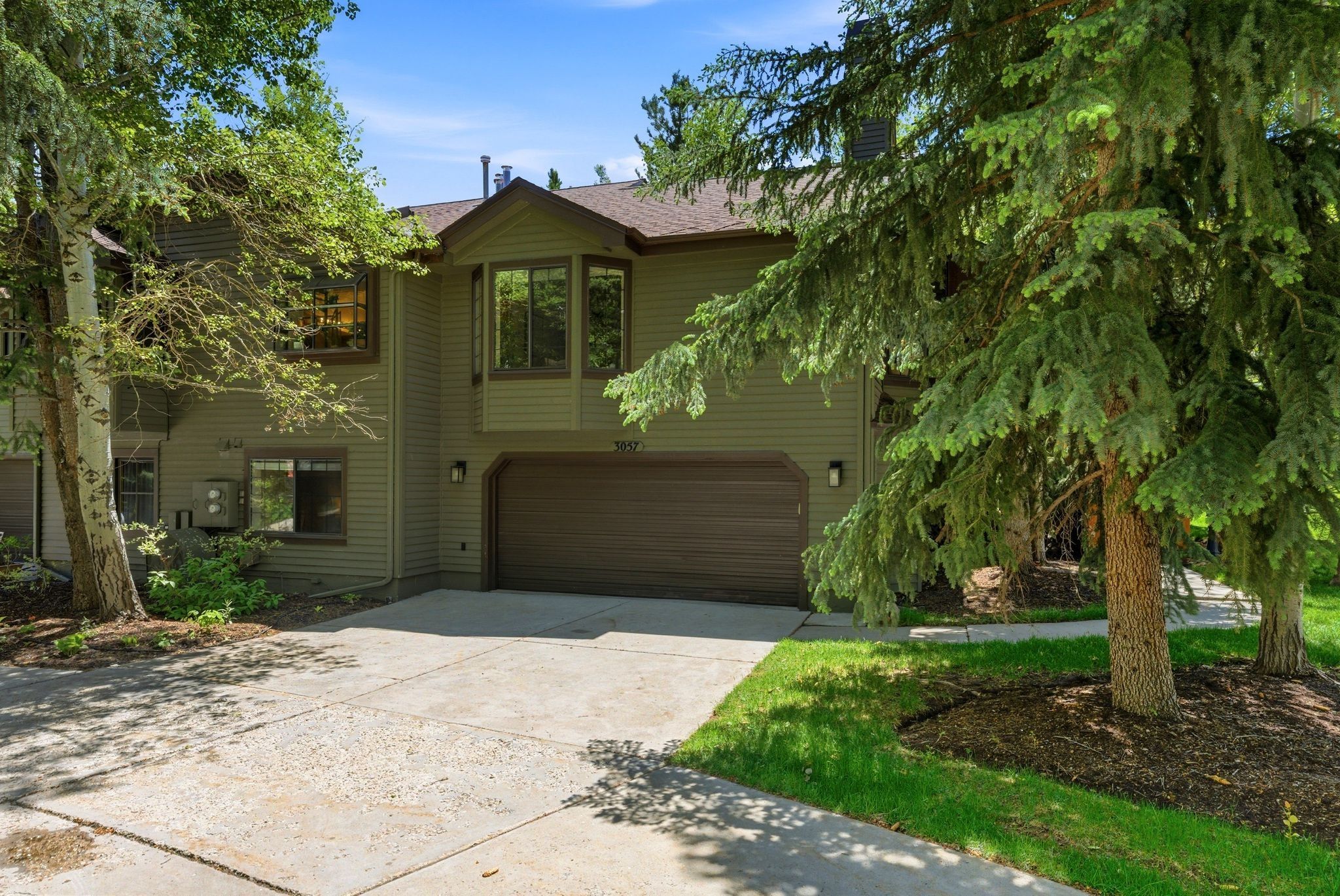 Two-story exterior with horizontal siding, an integrated garage, a bay window, and mature trees