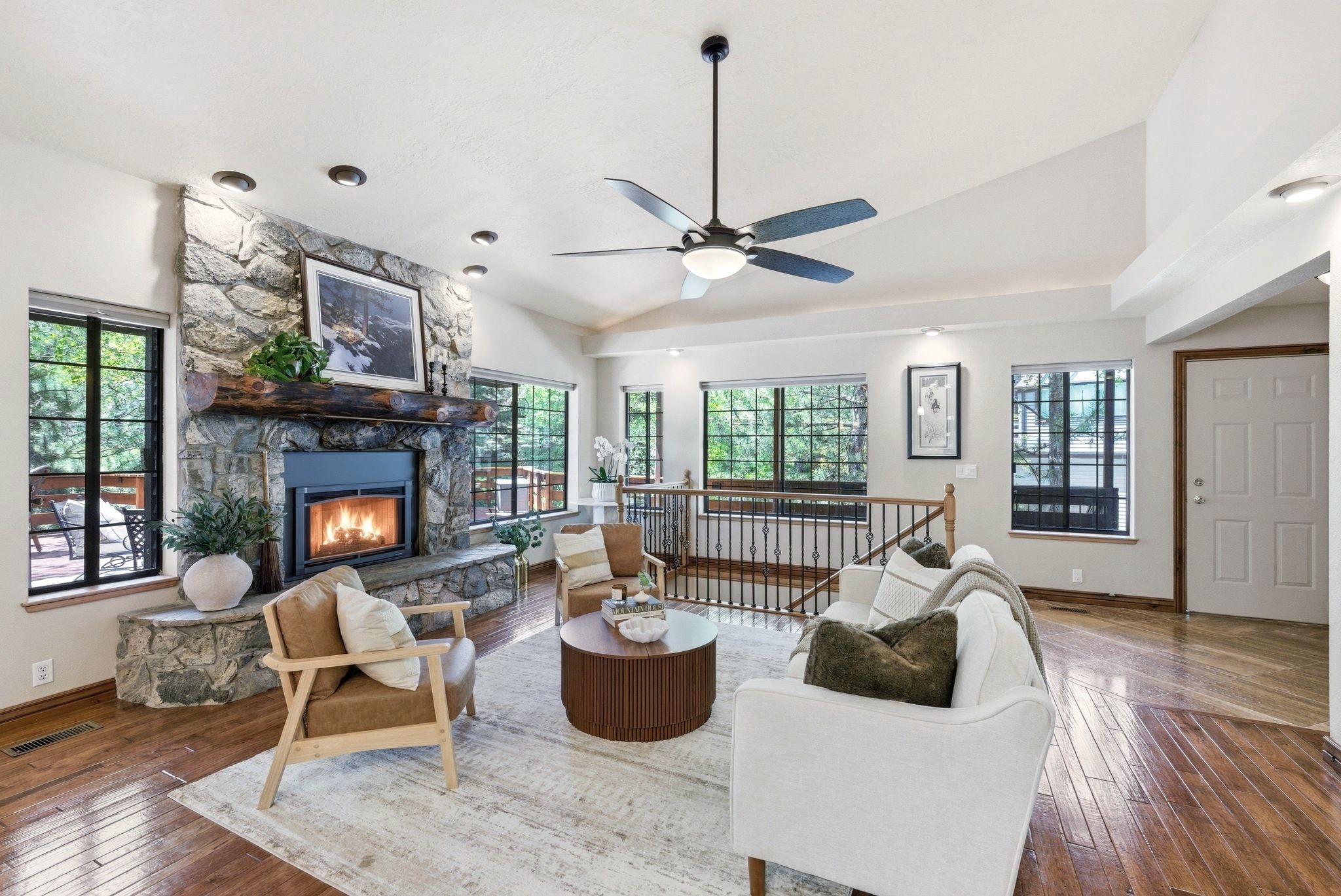 Spacious living area featuring a stone-clad fireplace with wood mantel, vaulted ceilings, recessed lighting, and hardwood flooring