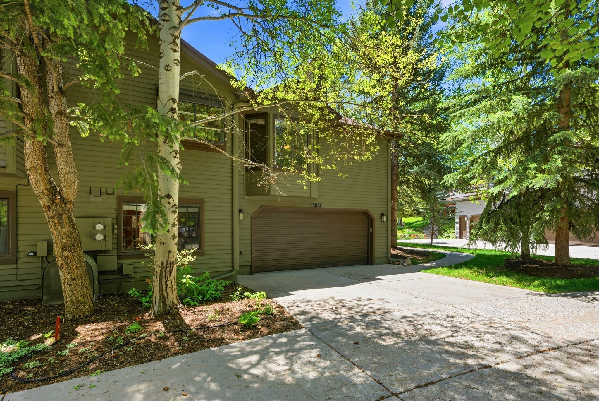 Exterior featuring horizontal siding, an integrated garage, a concrete driveway, established trees, and surrounding greenery