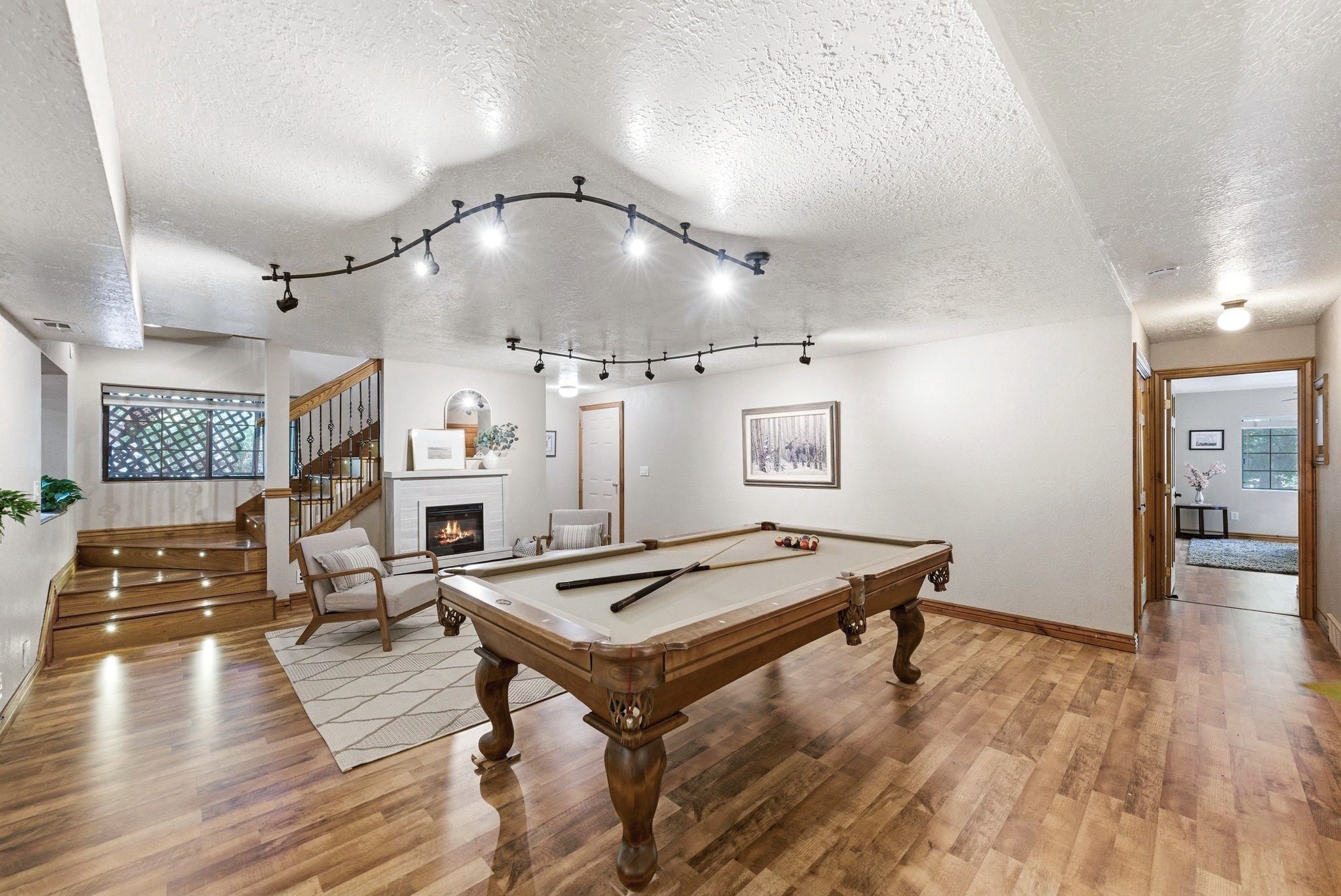 Versatile entertainment space featuring wood-finish flooring, a fireplace with a white surround, and track lighting