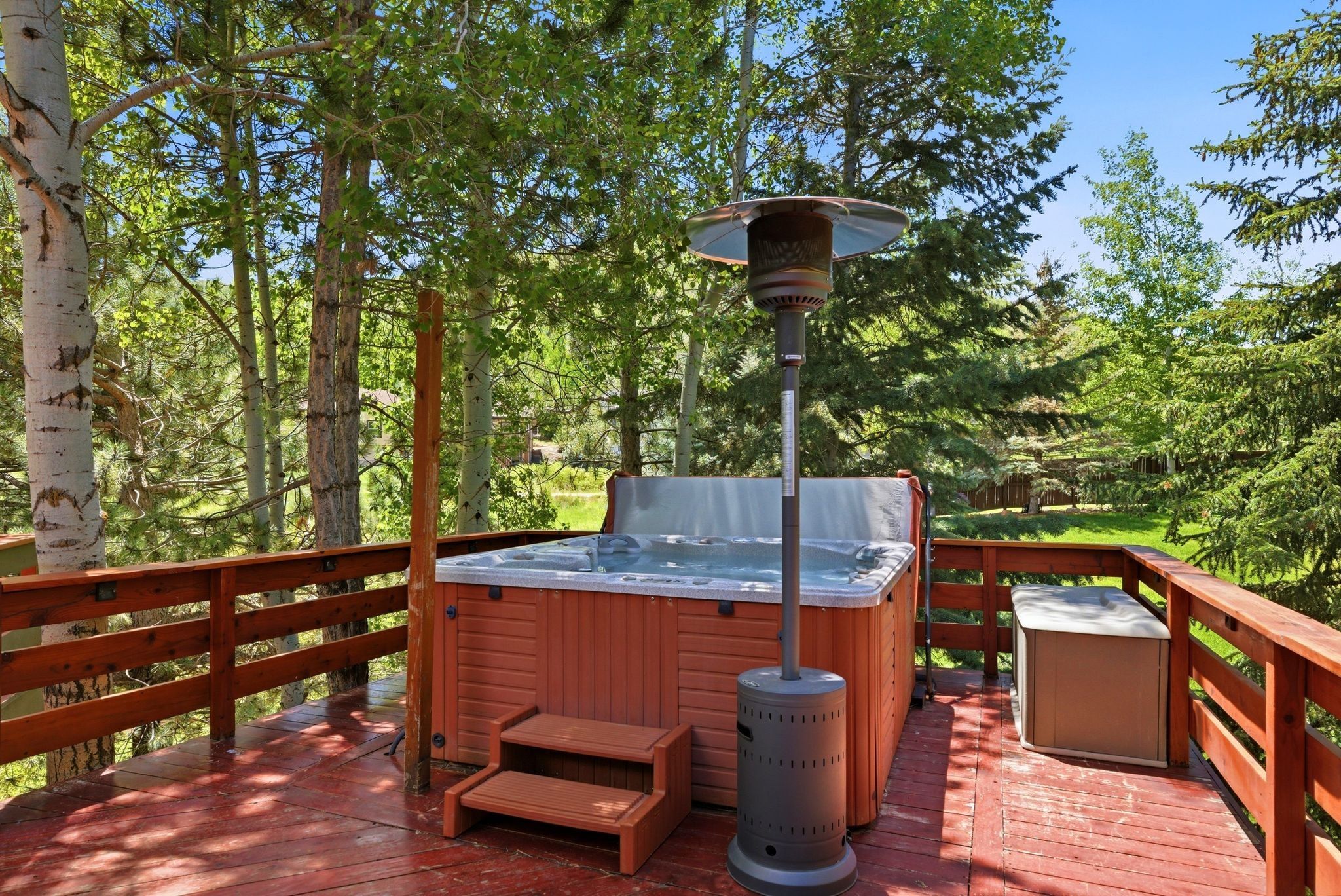 Spacious wooden deck featuring an integrated hot tub with accompanying steps, a protective railing, and surrounding mature trees