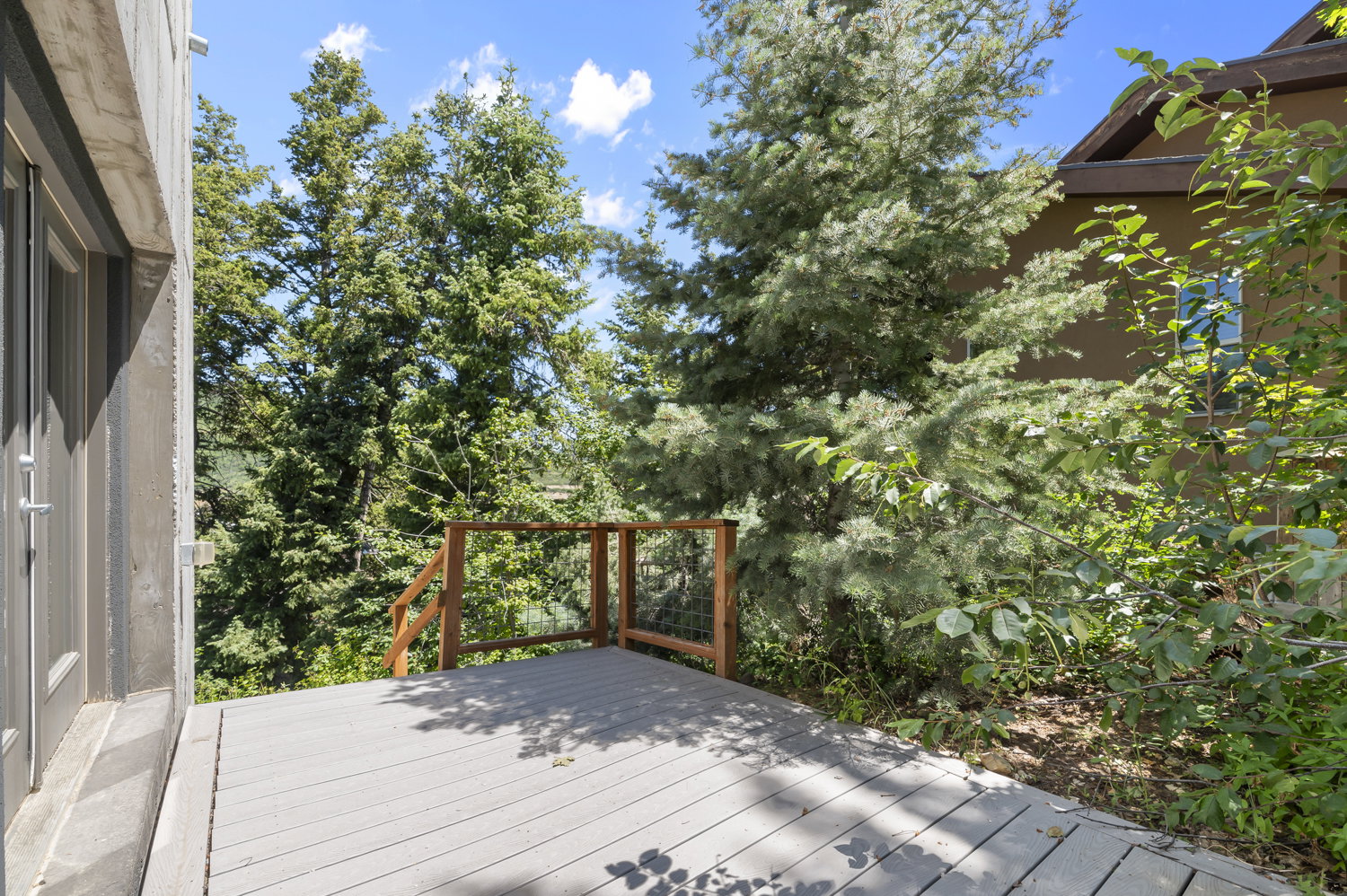 Outdoor deck featuring composite decking, wooden railings, and surrounding mature trees under a clear sky