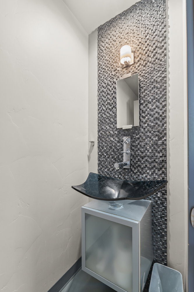 Powder room featuring a glass vessel sink, wall-mounted faucet, and a mosaic tile accent wall with a wall sconce