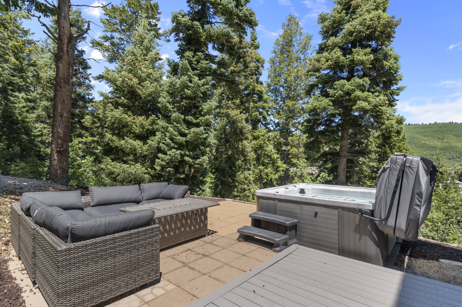 Expansive outdoor patio featuring a hot tub, tiled hardscaping, and a composite deck section