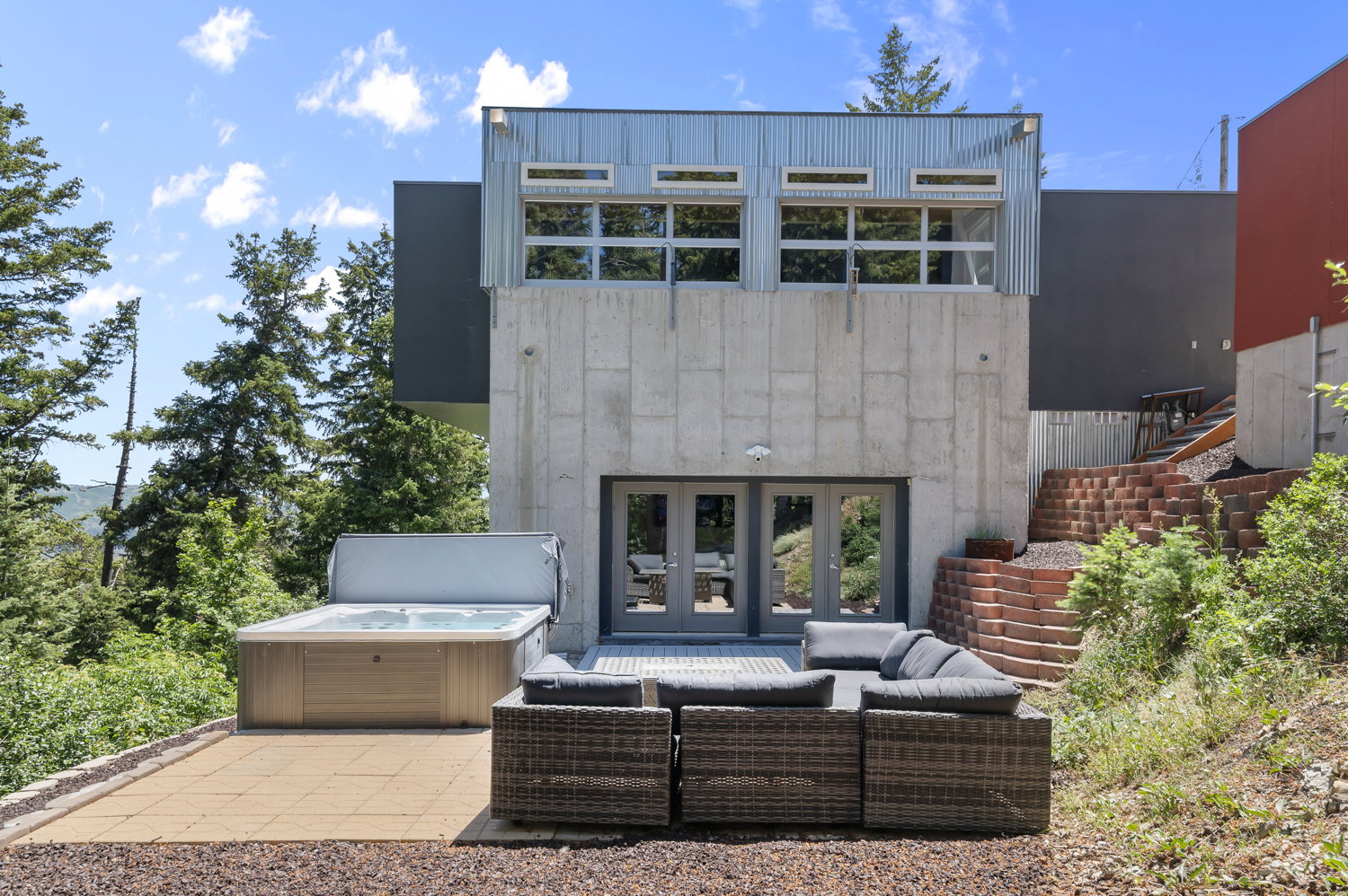 Modern exterior featuring concrete and corrugated metal siding, double glass doors, a paver patio, and terraced landscaping