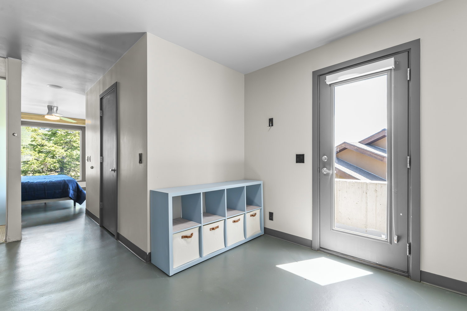 Light-filled interior space with a full-light exterior door, neutral wall tones, and gray trim