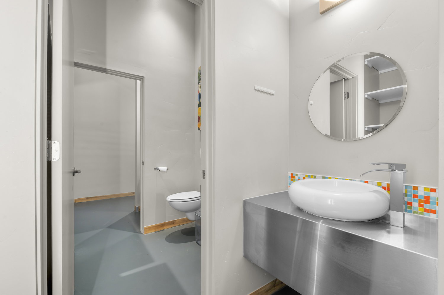Modern bathroom featuring a vessel sink, brushed metal vanity, and a mosaic tile backsplash