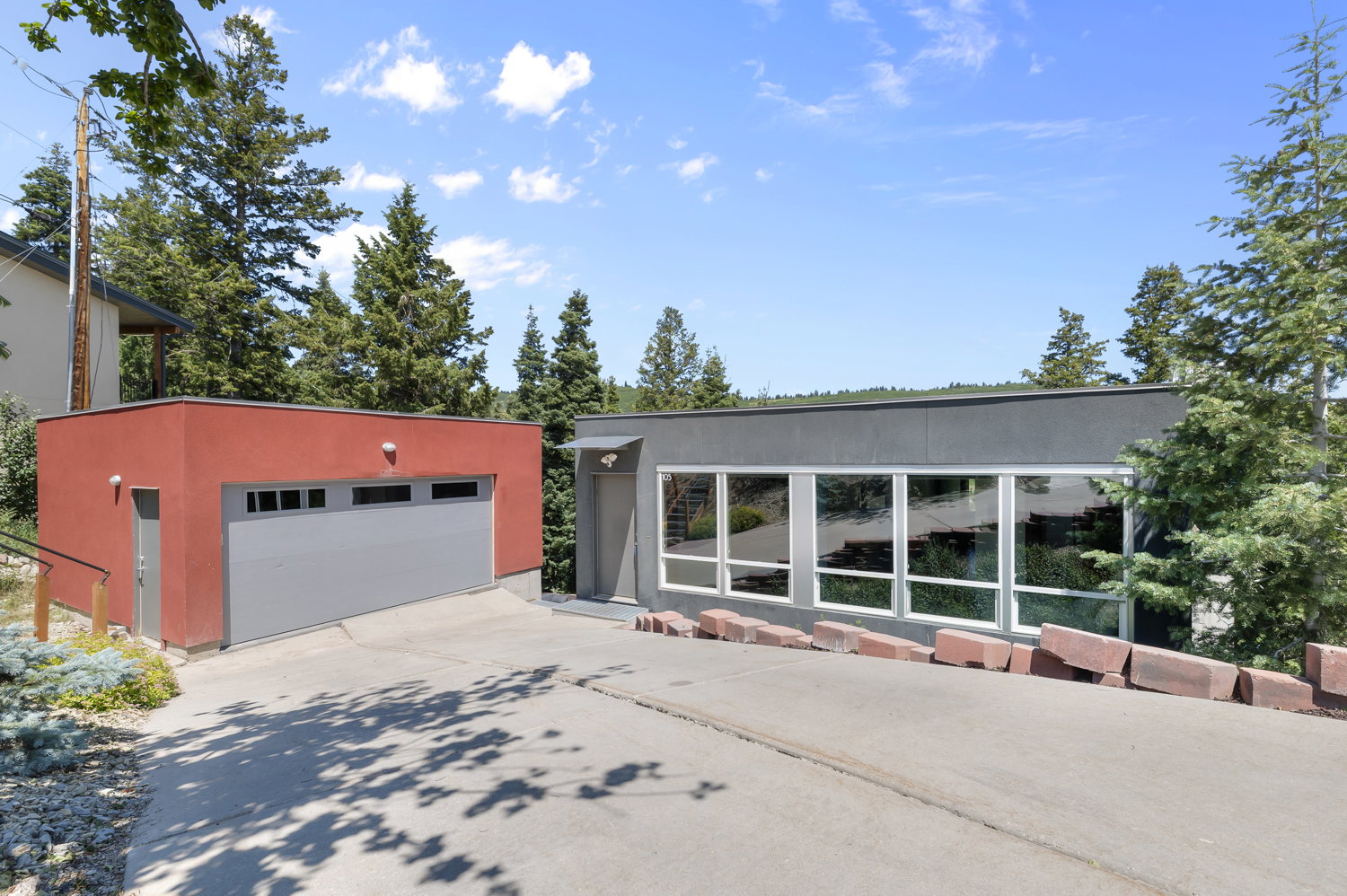 Modern exterior featuring a red detached garage with a gray garage door, a separate pedestrian door, and a gray main structure with expansive windows