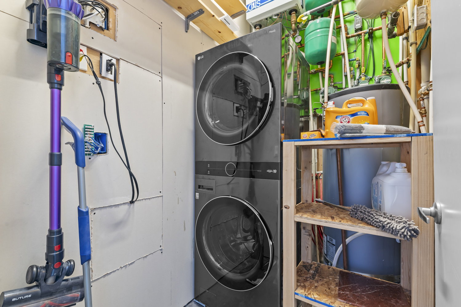 Laundry area featuring stacked washer and dryer units, exposed utility lines, and a built-in water heater