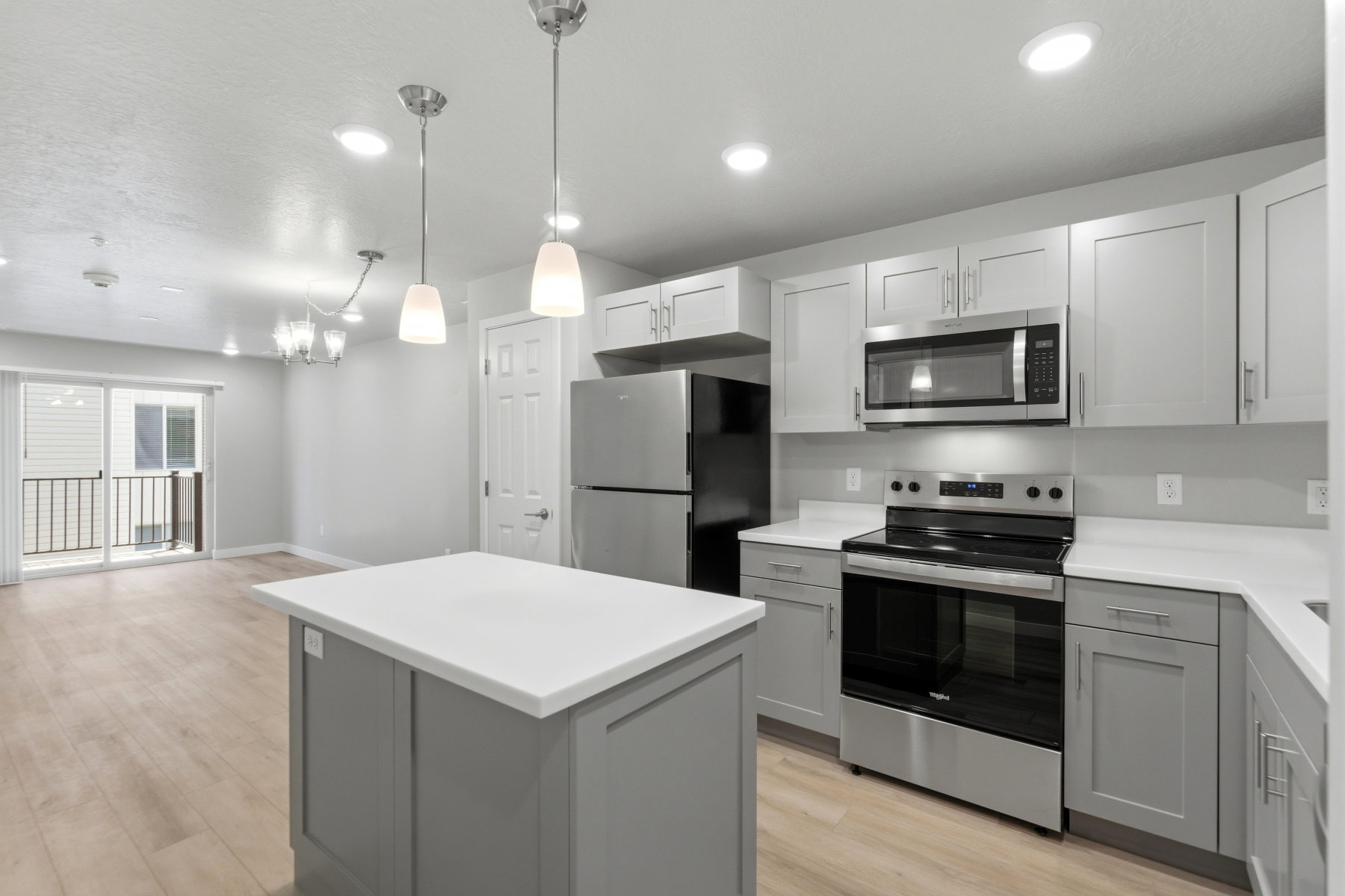 Modern kitchen featuring a central island with white countertop, light gray cabinetry, stainless steel appliances, and pendant lighting