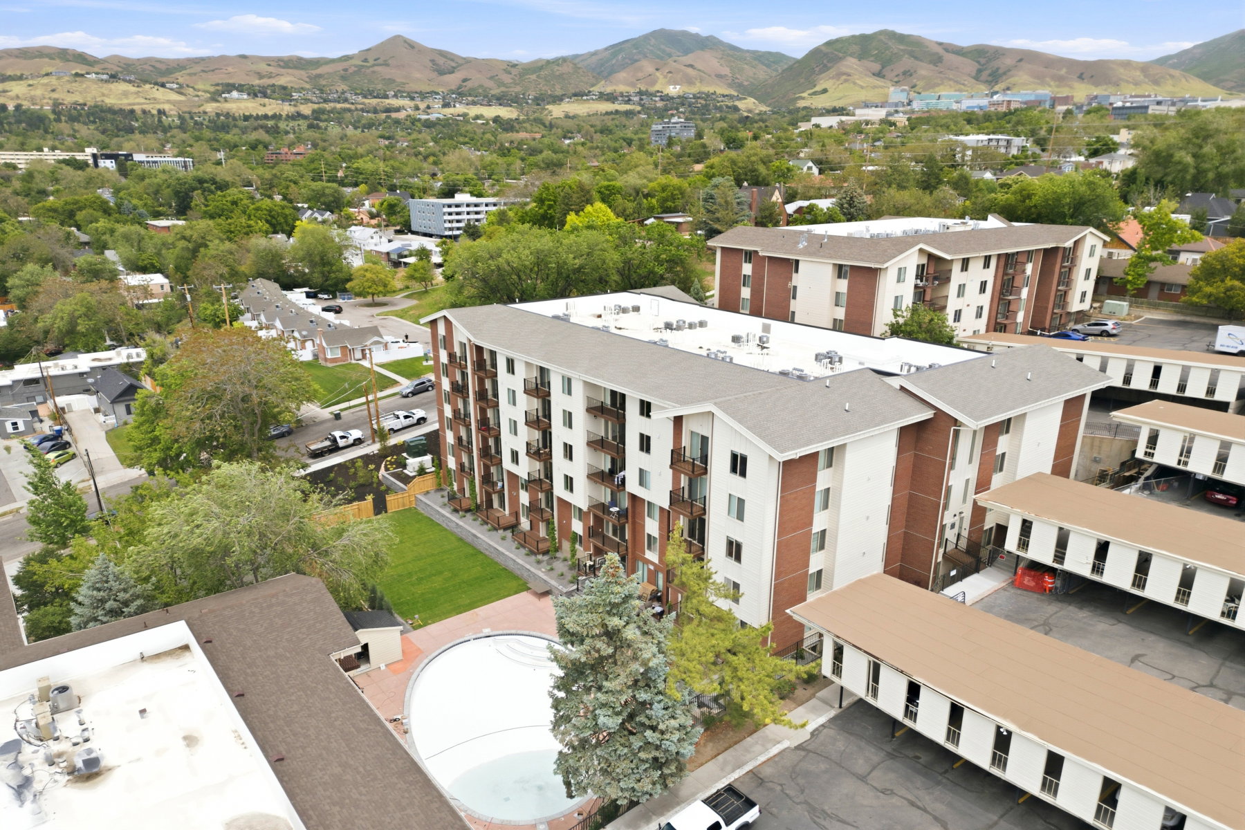 Multi-story residential buildings featuring brick and white siding, individual balconies, and a central green space with an outdoor swimming pool