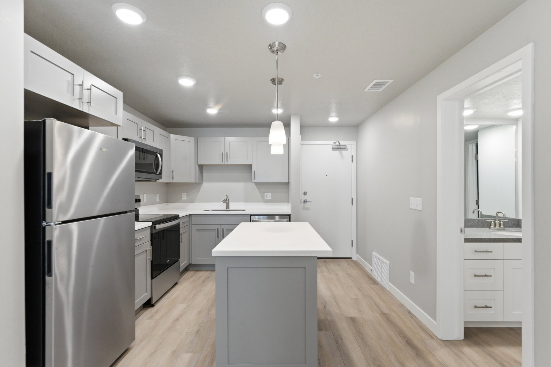 Modern kitchen featuring light gray cabinetry, stainless steel appliances, a center island with a white countertop, and wood-finish flooring