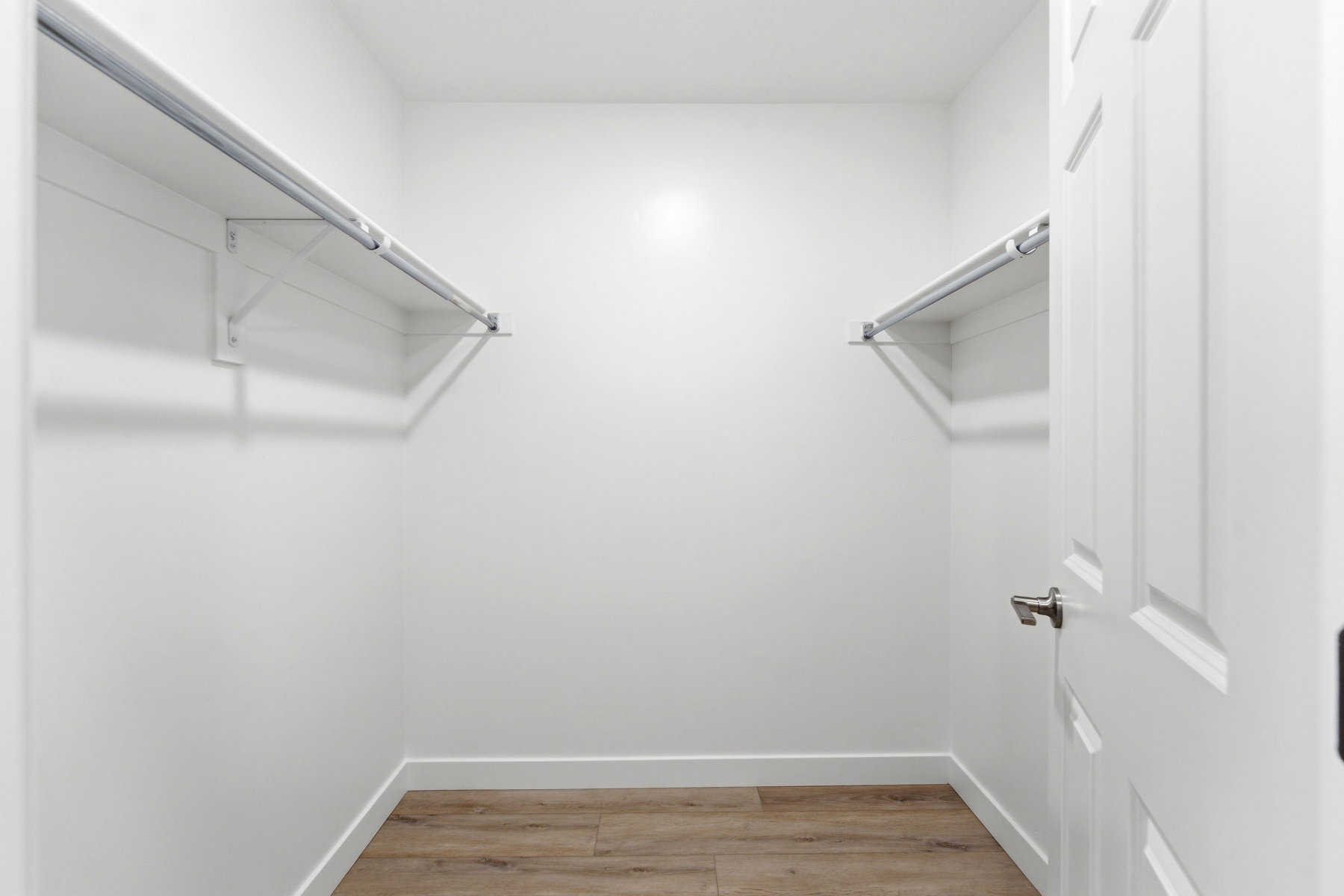 Walk-in closet featuring wood-finish flooring, white walls, and dual clothing rods with shelving