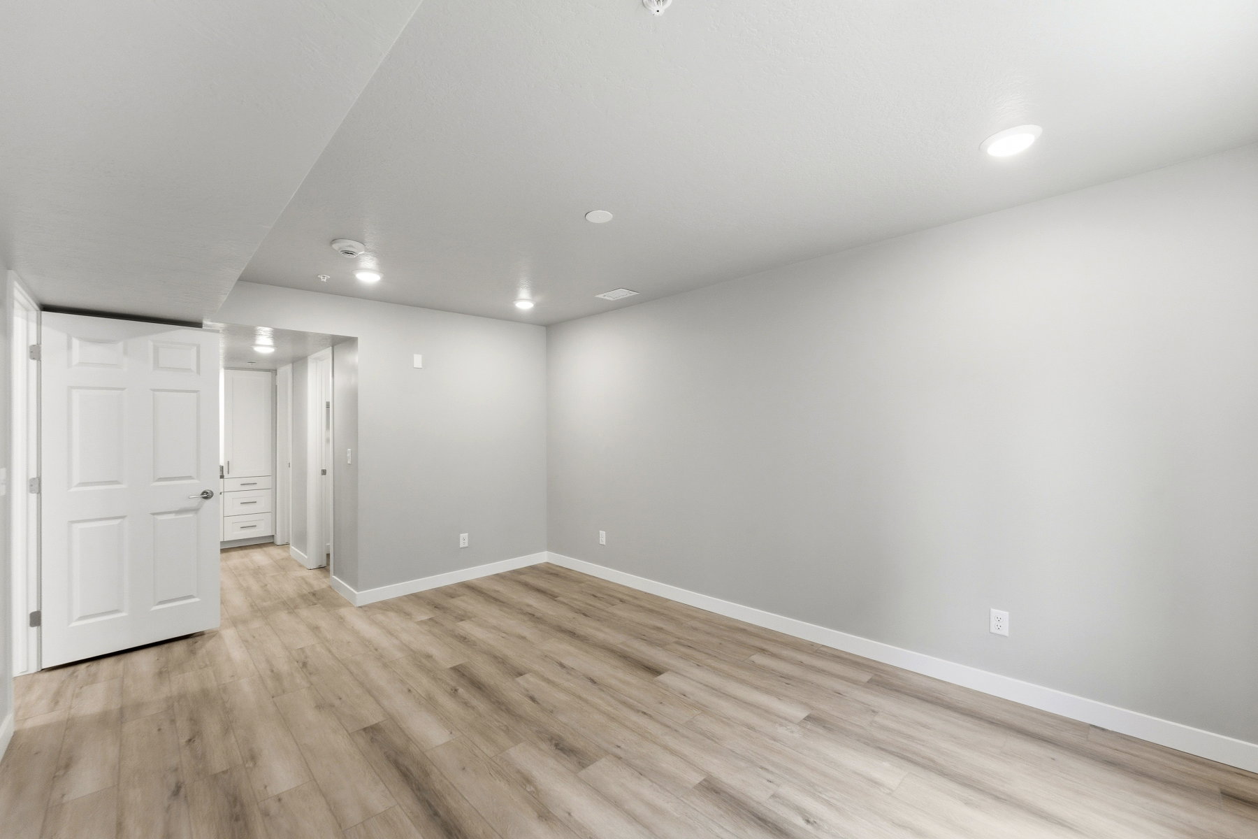Spacious room with light wood-finish flooring, recessed lighting, neutral gray walls, and white baseboards