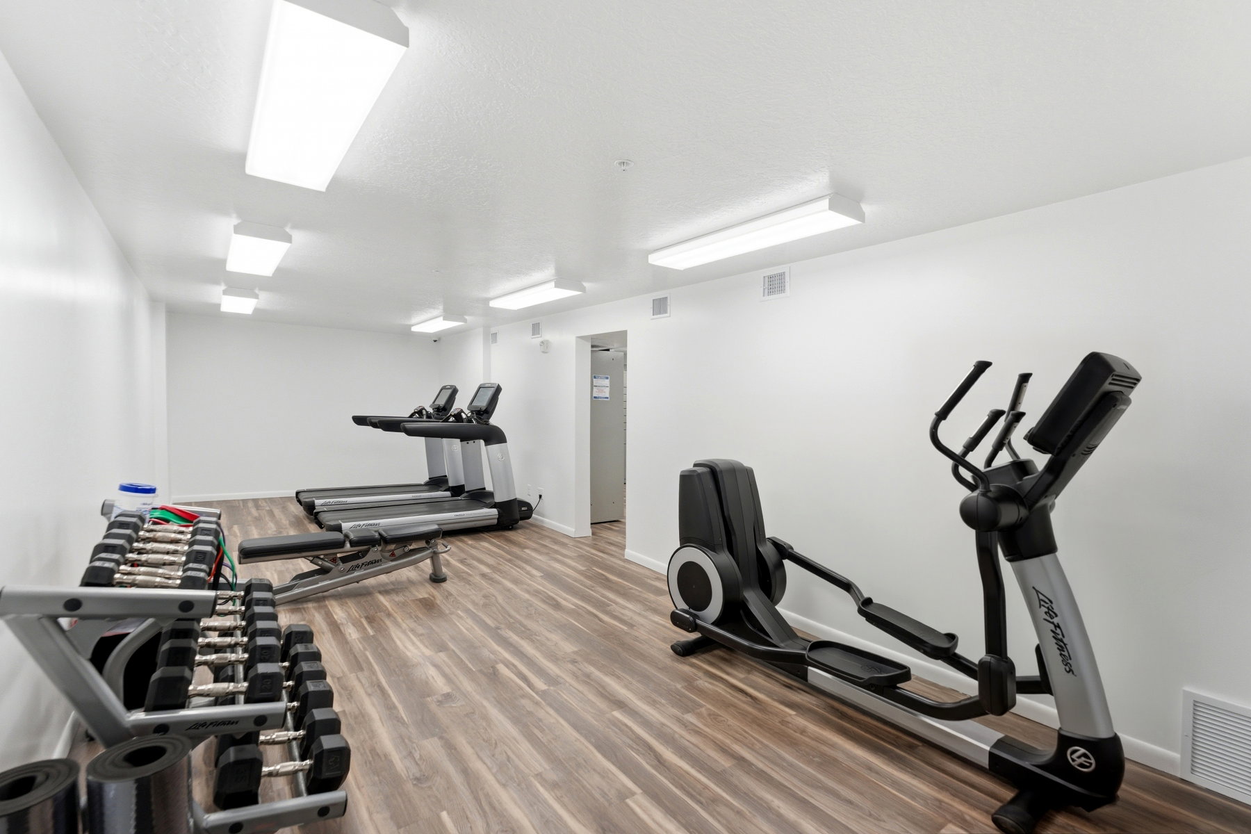 Dedicated fitness room featuring wood-finish flooring, white walls, and bright overhead lighting