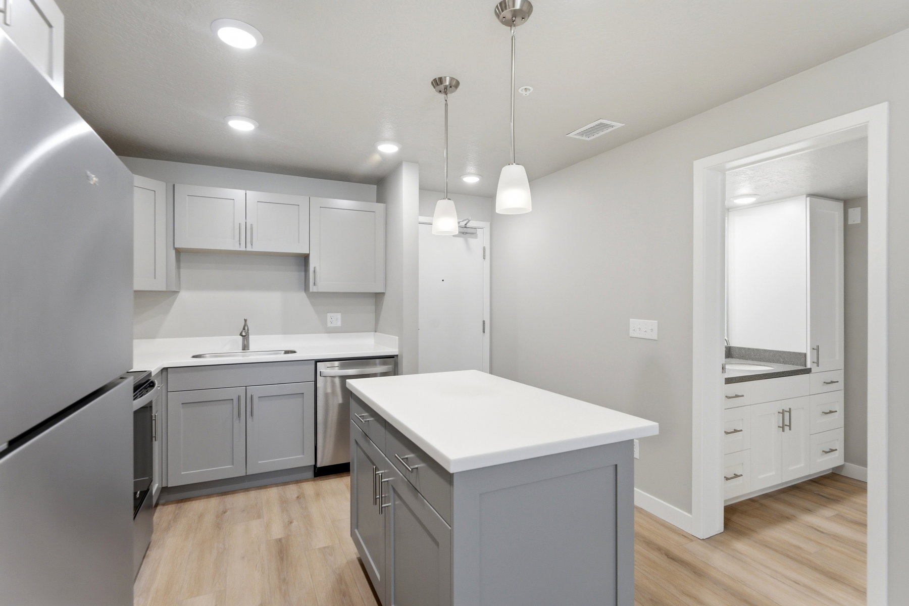 Contemporary kitchen featuring light gray cabinetry, white countertops, stainless steel appliances, and wood-finish flooring