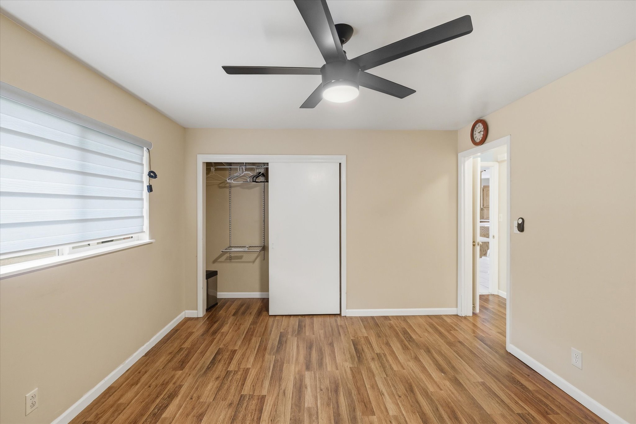 Spacious room featuring wood-finish flooring, a modern ceiling fan with integrated lighting, a window with horizontal blinds, and a closet with sliding doors