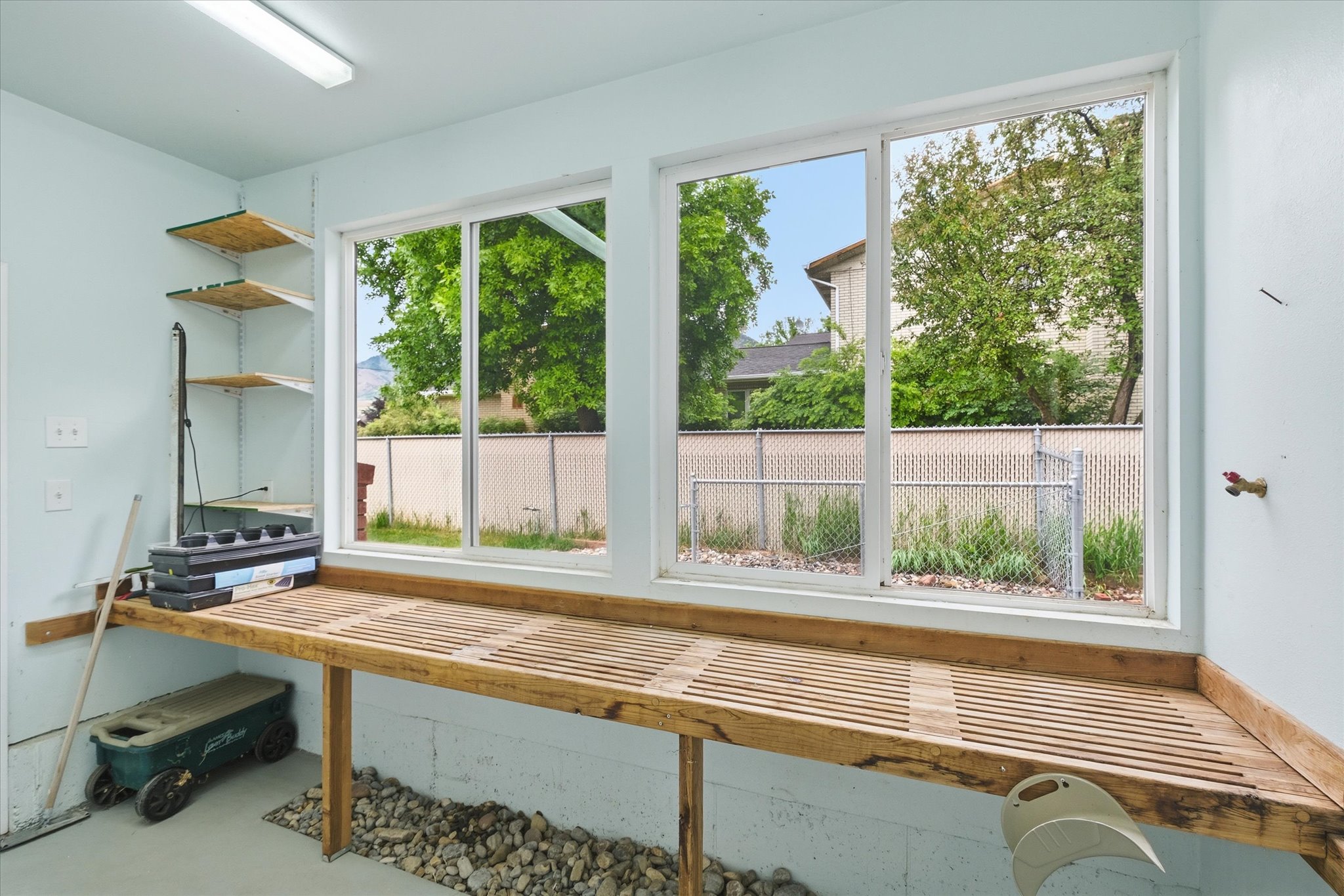 Utility room featuring a slatted wood-finish workbench, adjustable wall shelving, and two large windows
