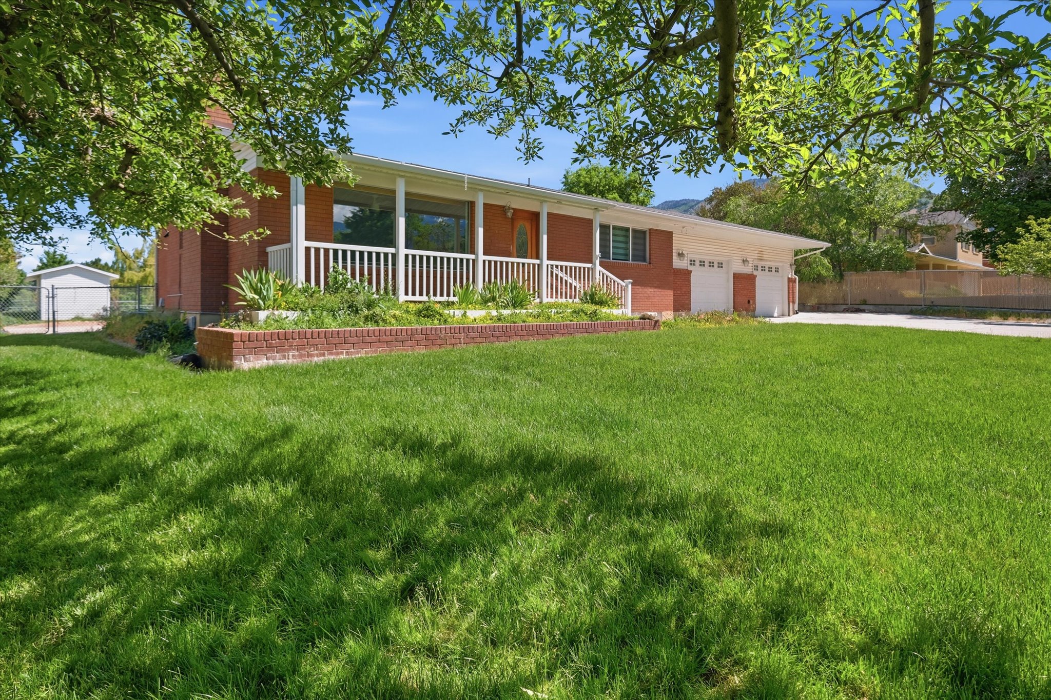 Brick exterior featuring a covered porch with white railings, a three-car garage, and a expansive front lawn