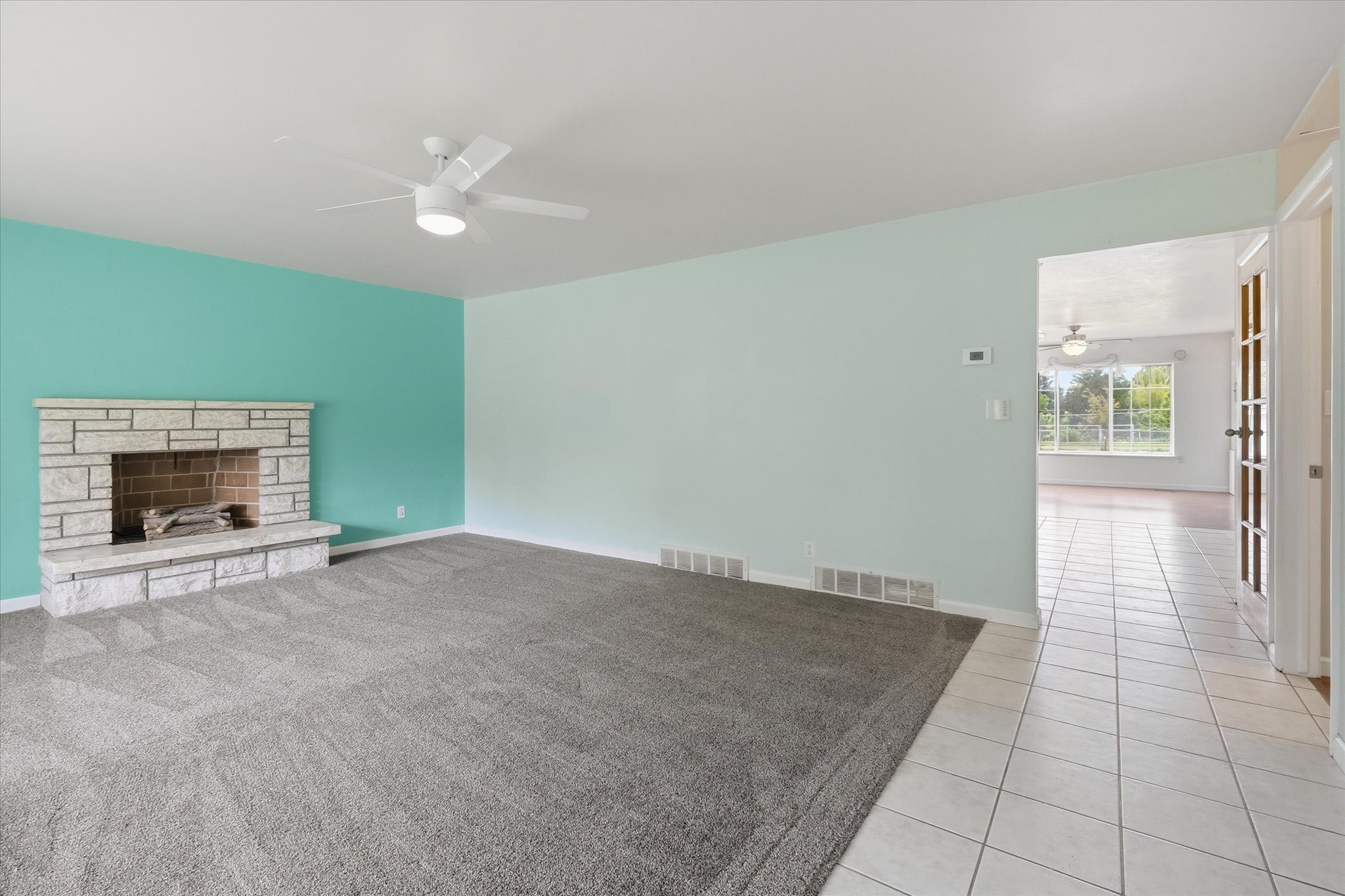 Living space featuring a stone fireplace with hearth, ceiling fan, and carpet flooring