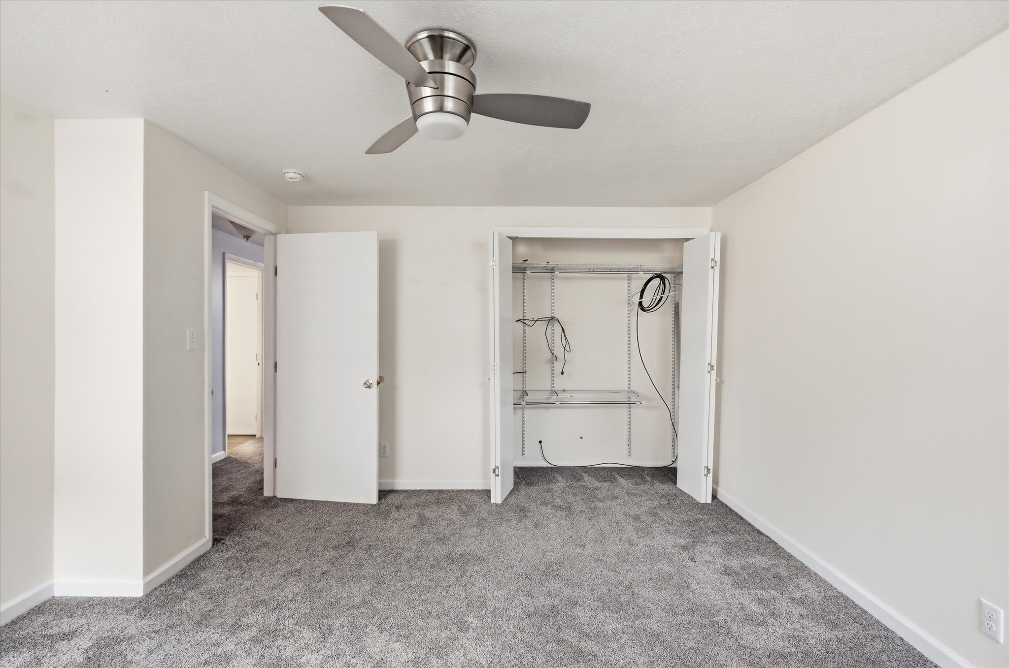 Neutral gray carpeting and white walls in this room with a ceiling fan