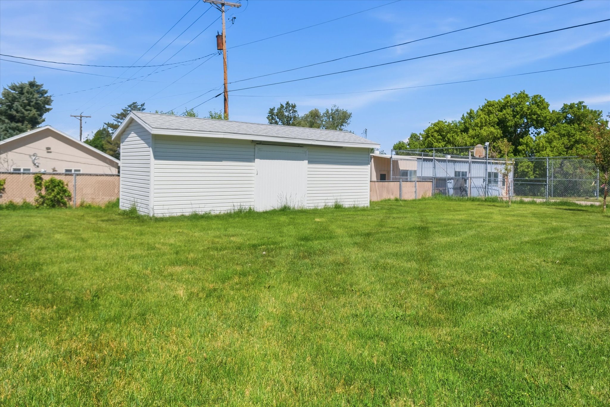 Expansive grassy yard featuring a white storage shed with a gabled roof