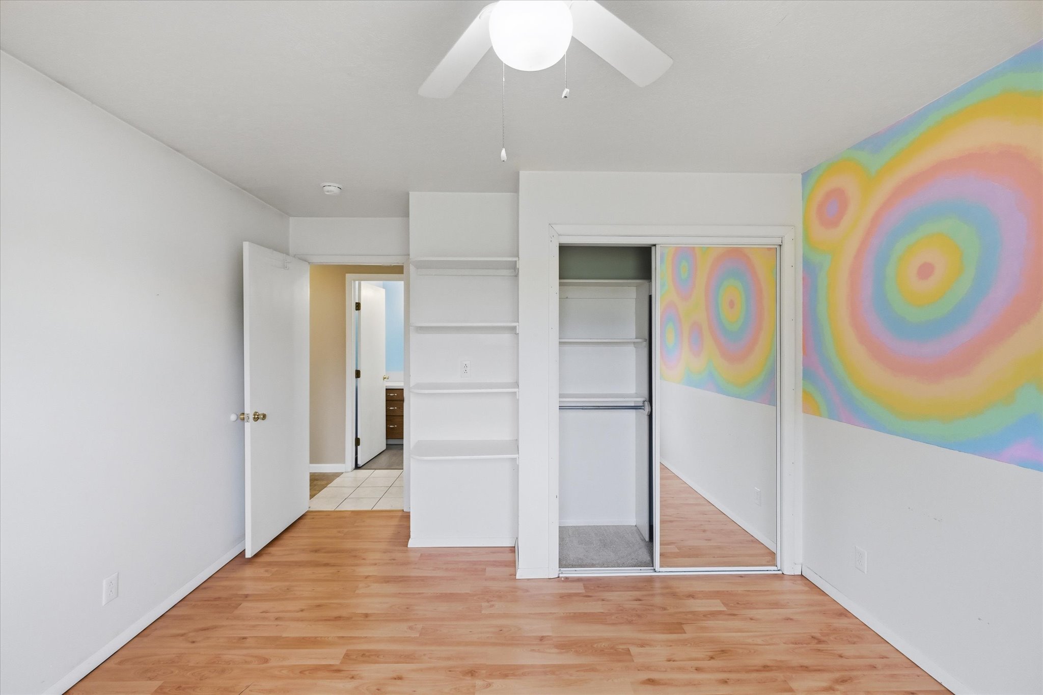 Room featuring wood-finish flooring, a ceiling fan, a built-in shelving unit, and a closet with mirrored sliding doors