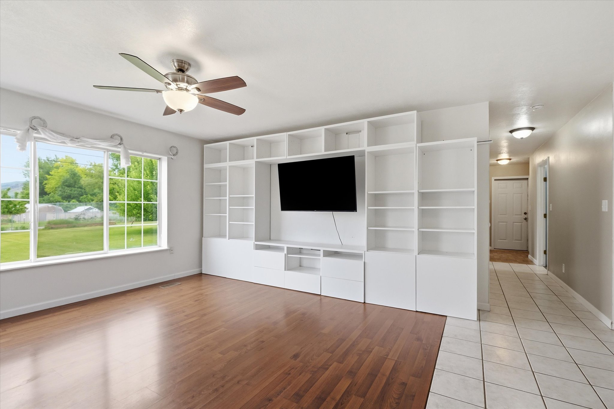Living space featuring wood-finish flooring, a large multi-pane window, and a built-in shelving unit with media storage