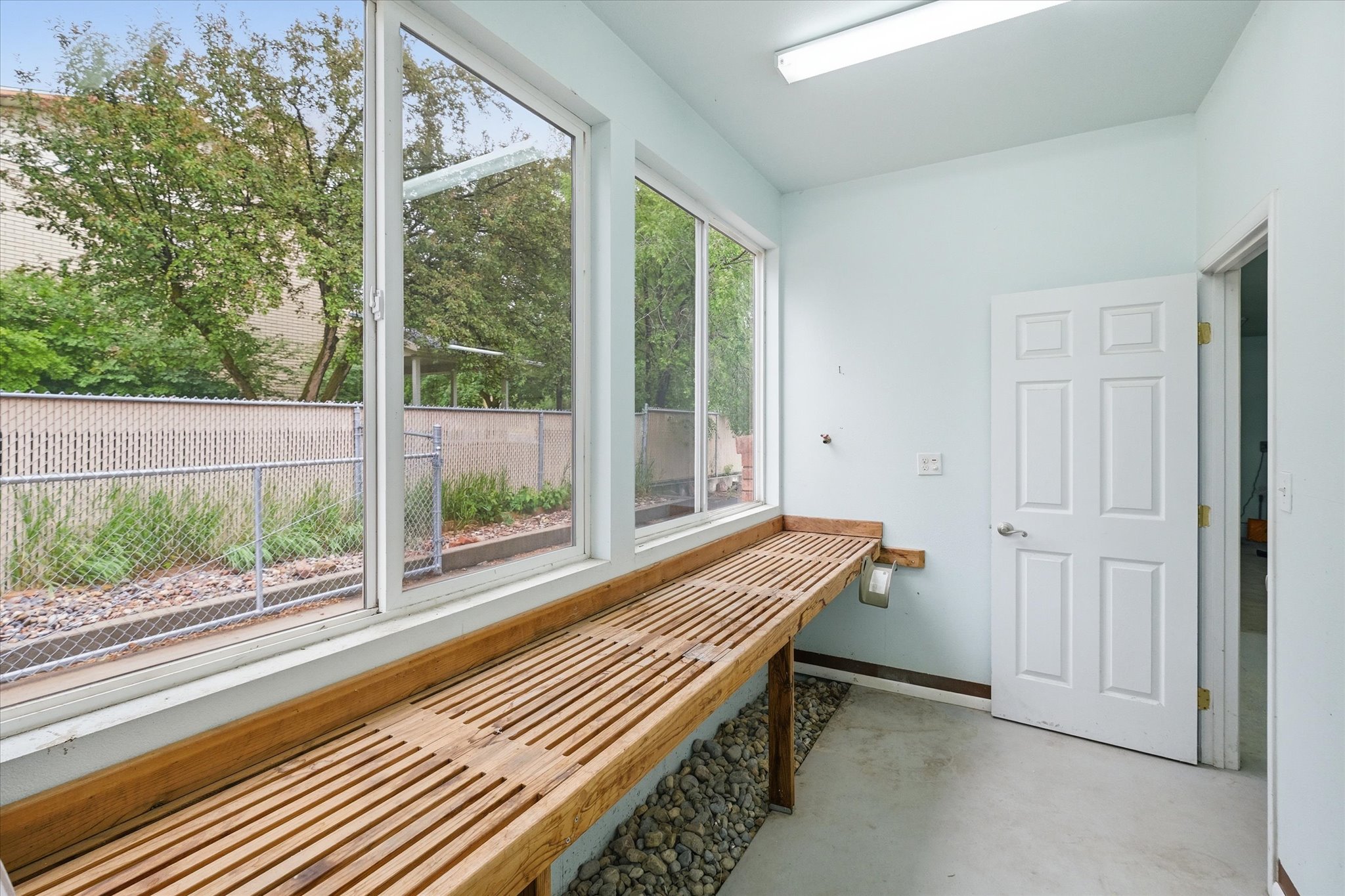 Bright room featuring a series of large windows, a built-in slatted wood-finish workbench, and an interior door