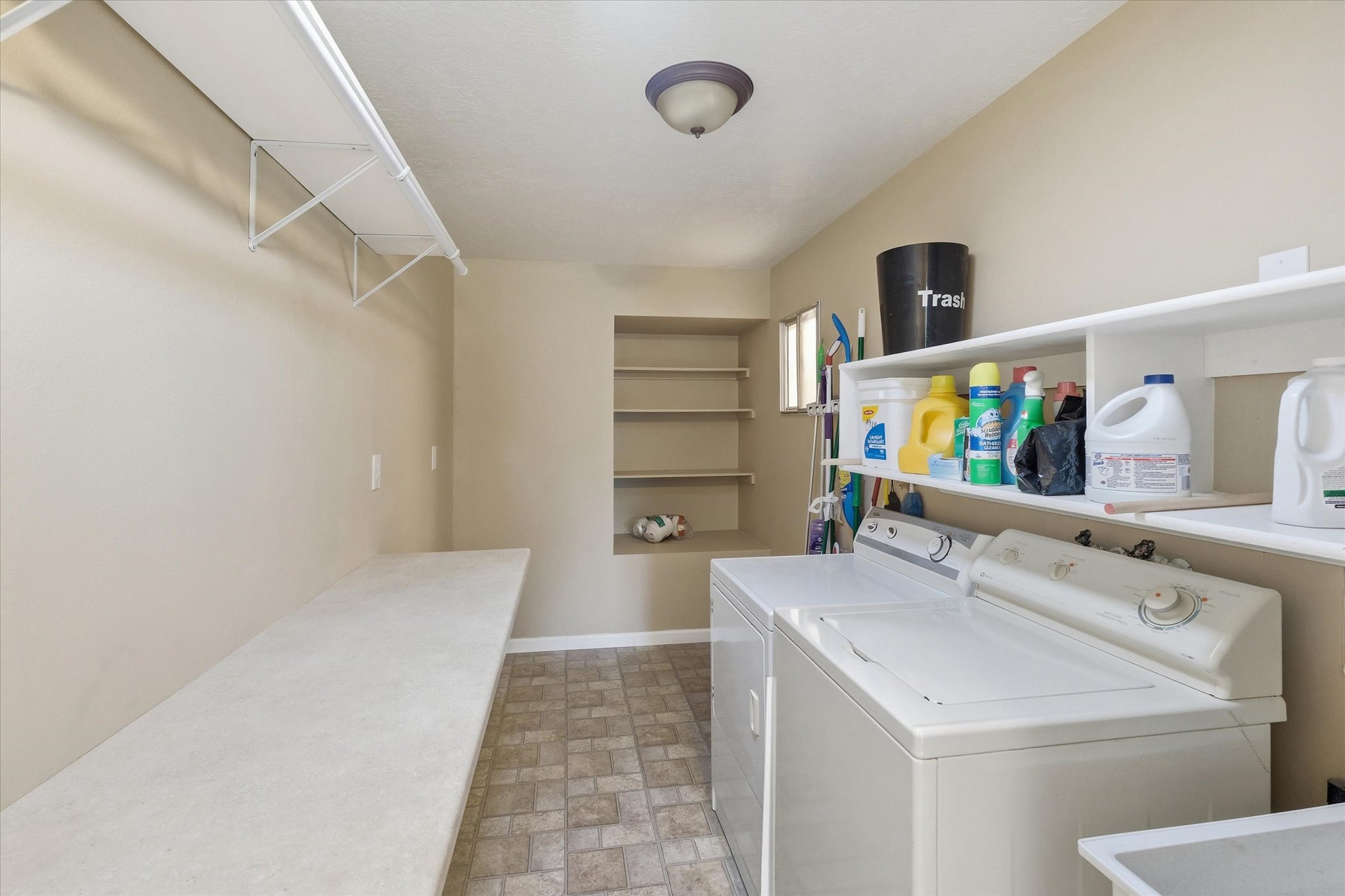 Dedicated laundry room featuring an overhead light fixture, built-in shelving, a long countertop, and patterned floor tile