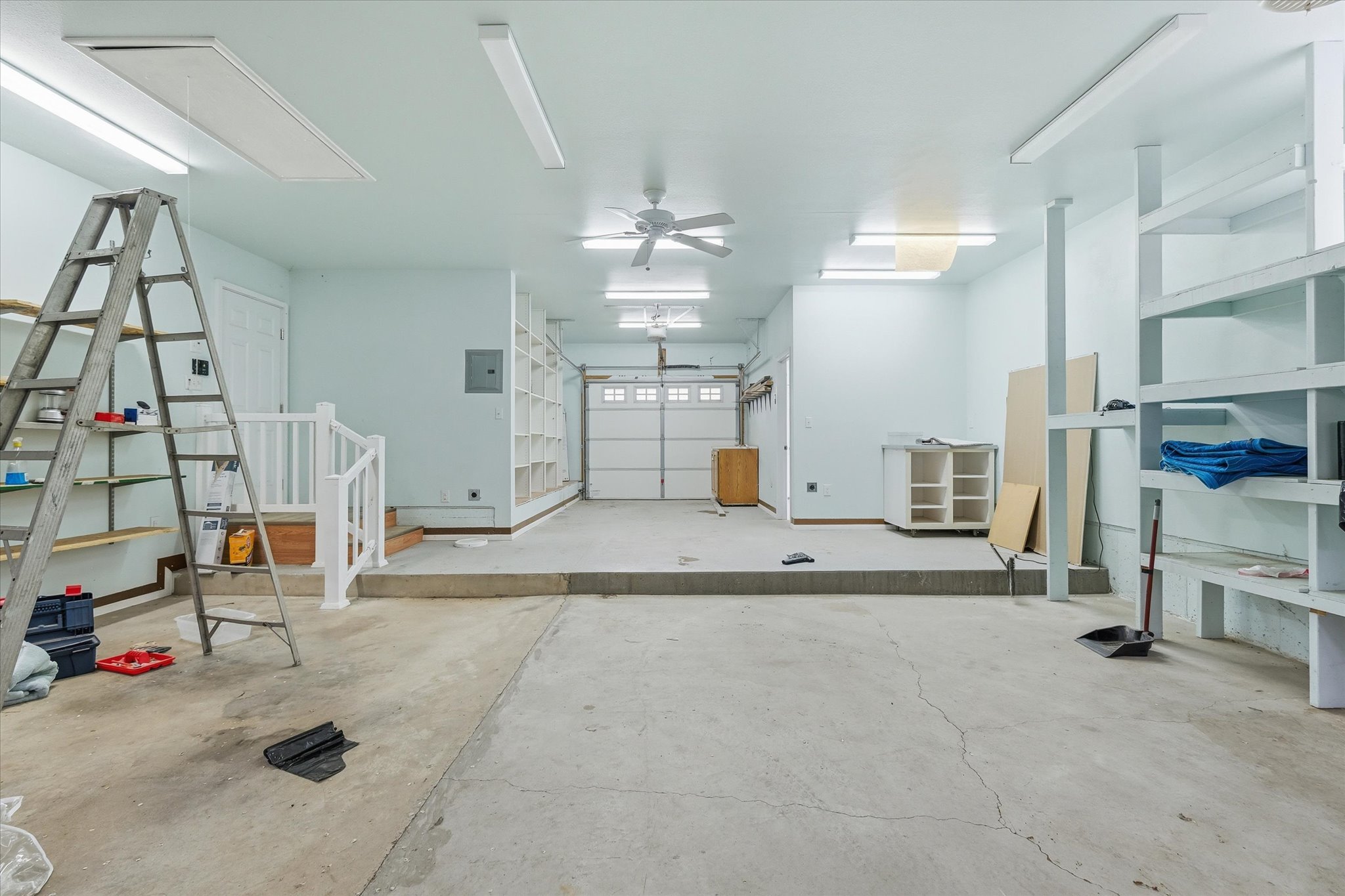 Concrete flooring, built-in shelving, white railing, overhead lighting, and a ceiling fan