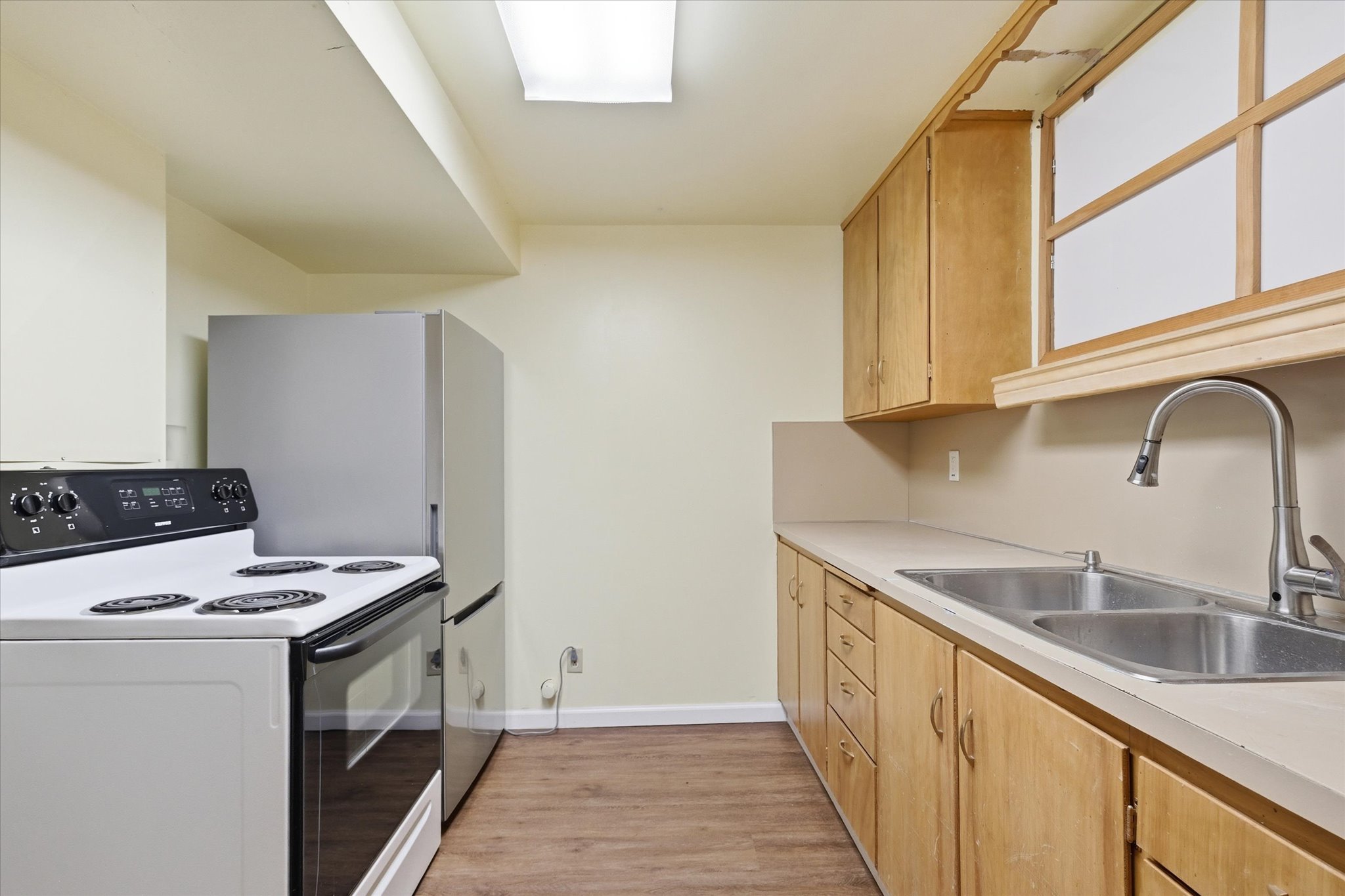Kitchen featuring wood-finish flooring, light tone cabinetry, a dual basin stainless steel sink with a gooseneck faucet, and white appliances