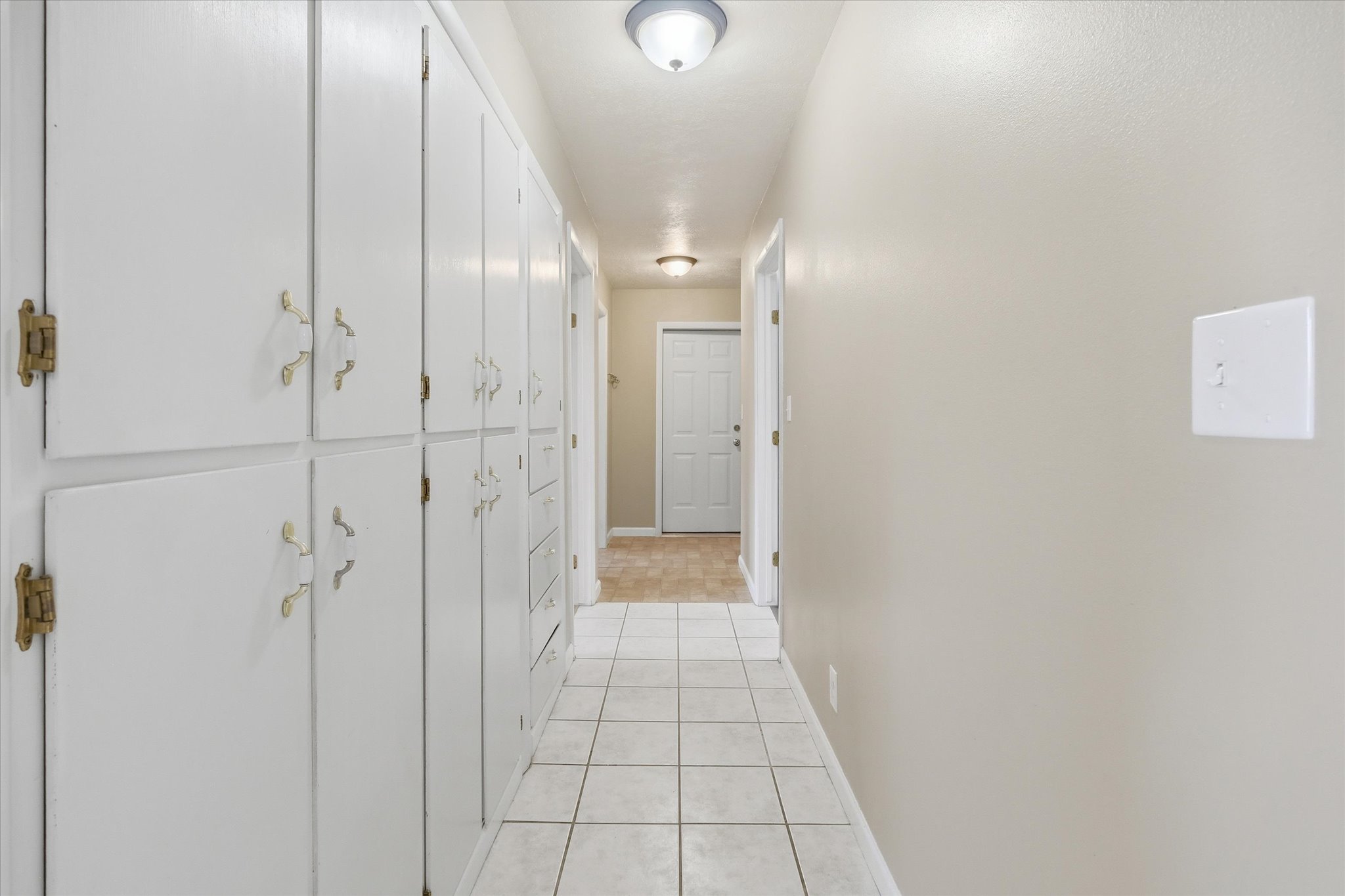 Hallway featuring extensive built-in white cabinetry with brass hardware, white tile flooring, neutral wall paint, and ceiling-mounted dome light fixtures