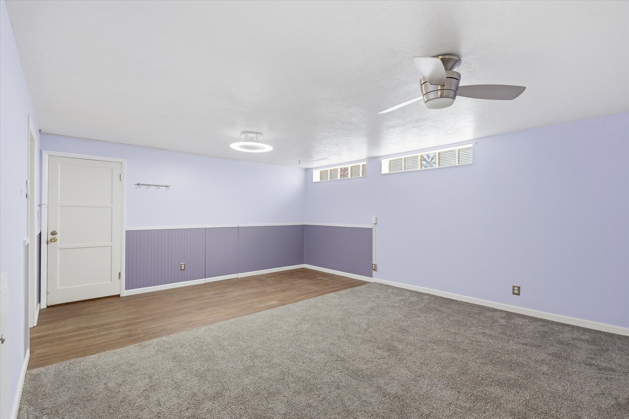 Spacious room featuring a partial wall of beadboard wainscoting, a ceiling fan, and recessed glass block windows