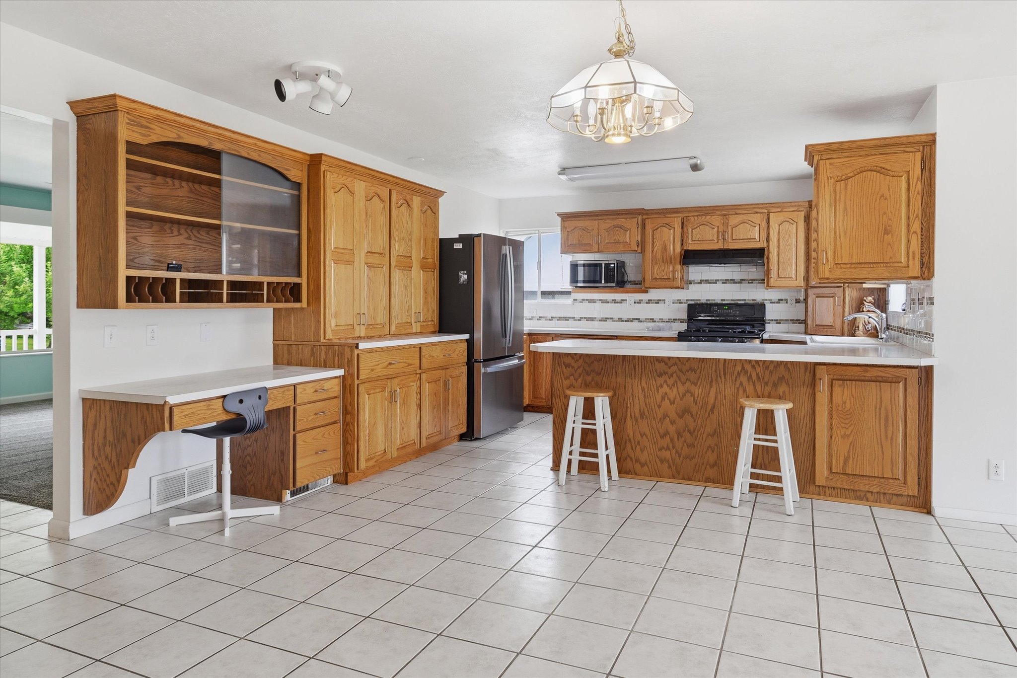 Spacious kitchen featuring extensive wood cabinetry, white tile flooring, durable countertops, and a built-in desk area