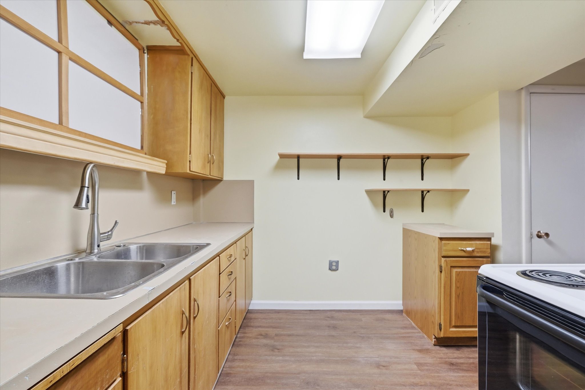 Kitchen featuring wood-finish flooring, light-toned cabinetry, a stainless steel double sink with a gooseneck faucet, light countertops, and open shelving