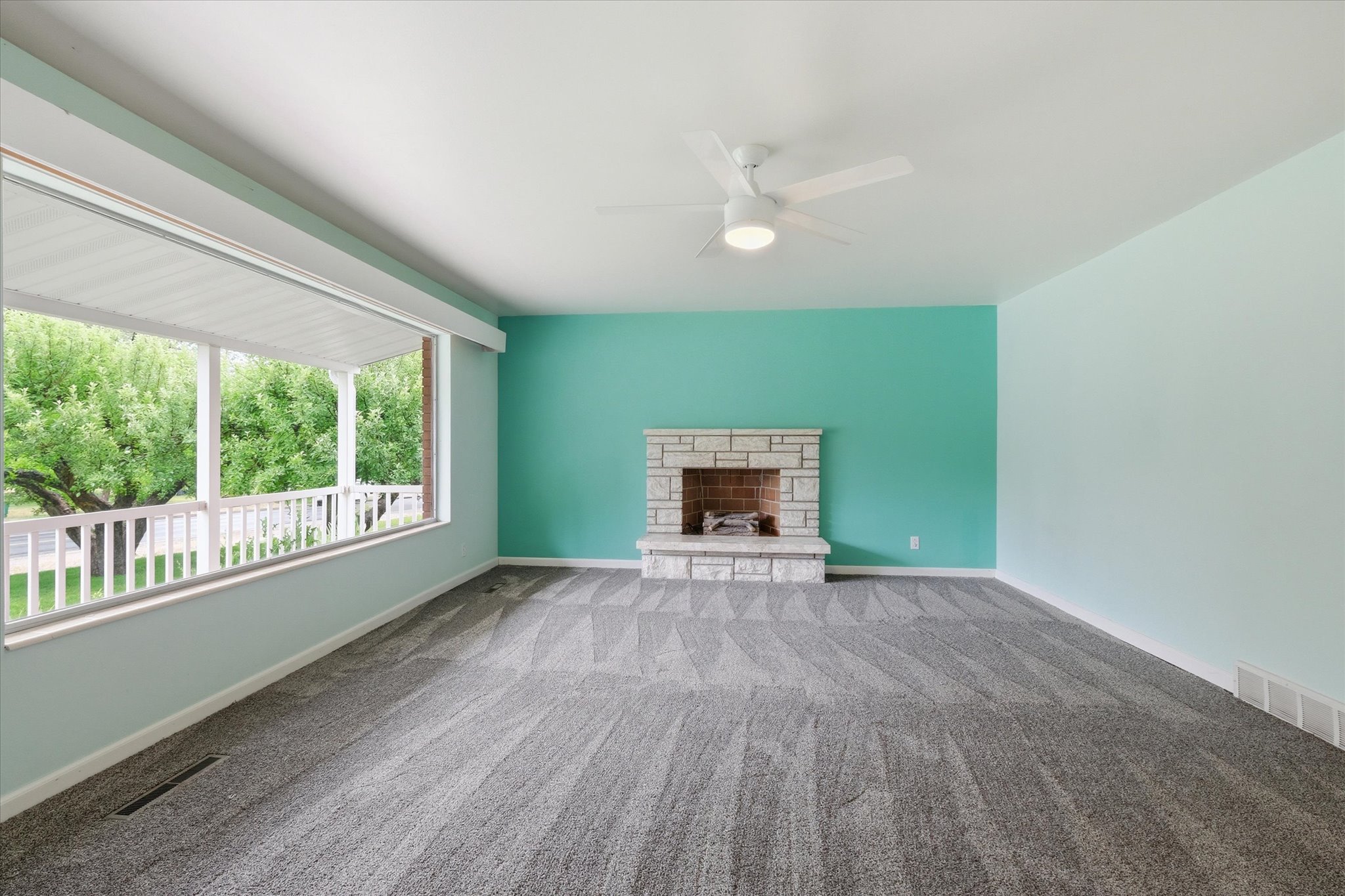 Spacious room featuring broadloom carpeting, a stone-faced fireplace with brick interior, and a ceiling fan with integrated lighting