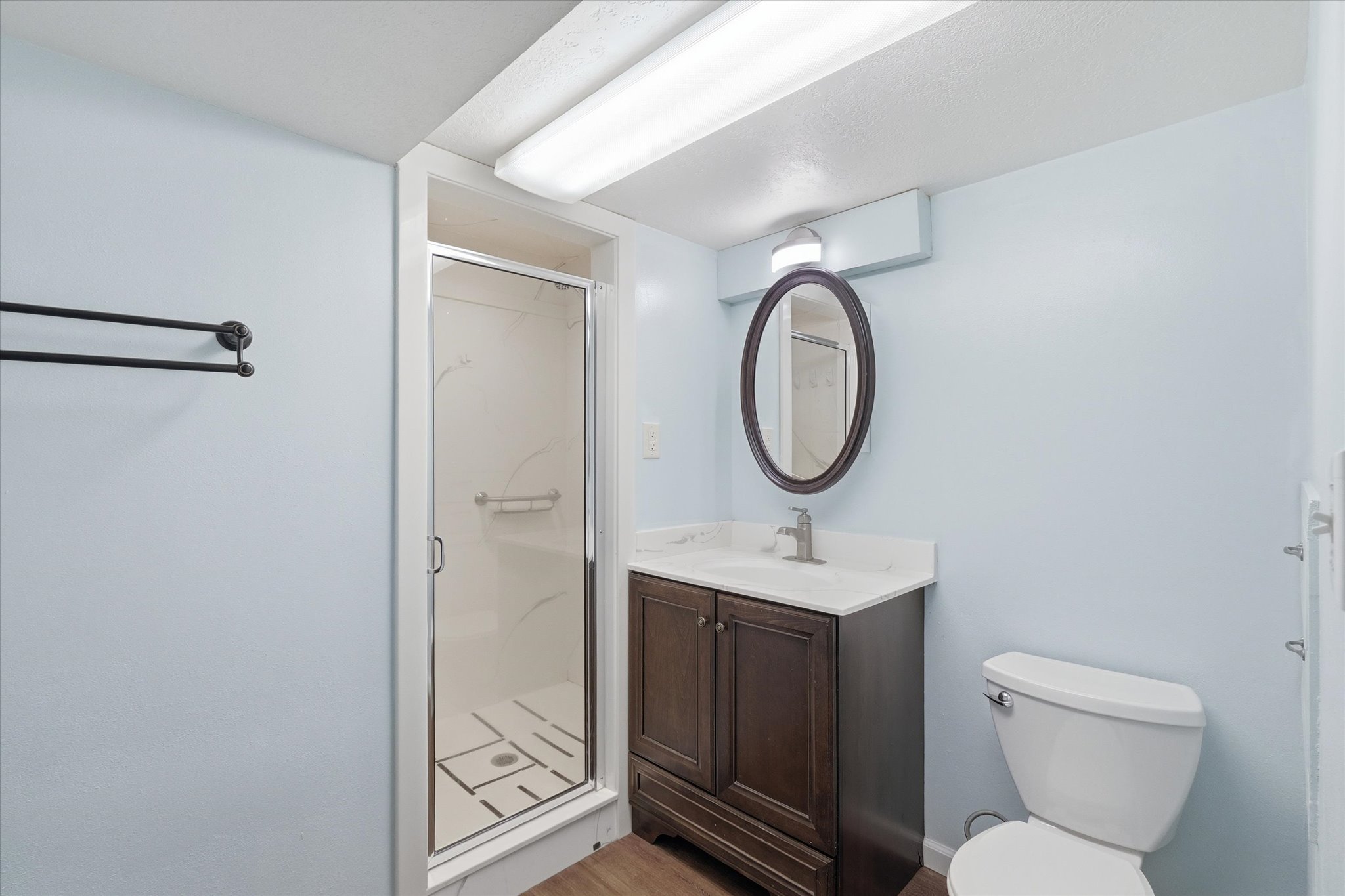 Bathroom featuring a stand-up shower with glass enclosure, single vanity with wood-finish cabinetry and white countertop, oval mirror, and commode
