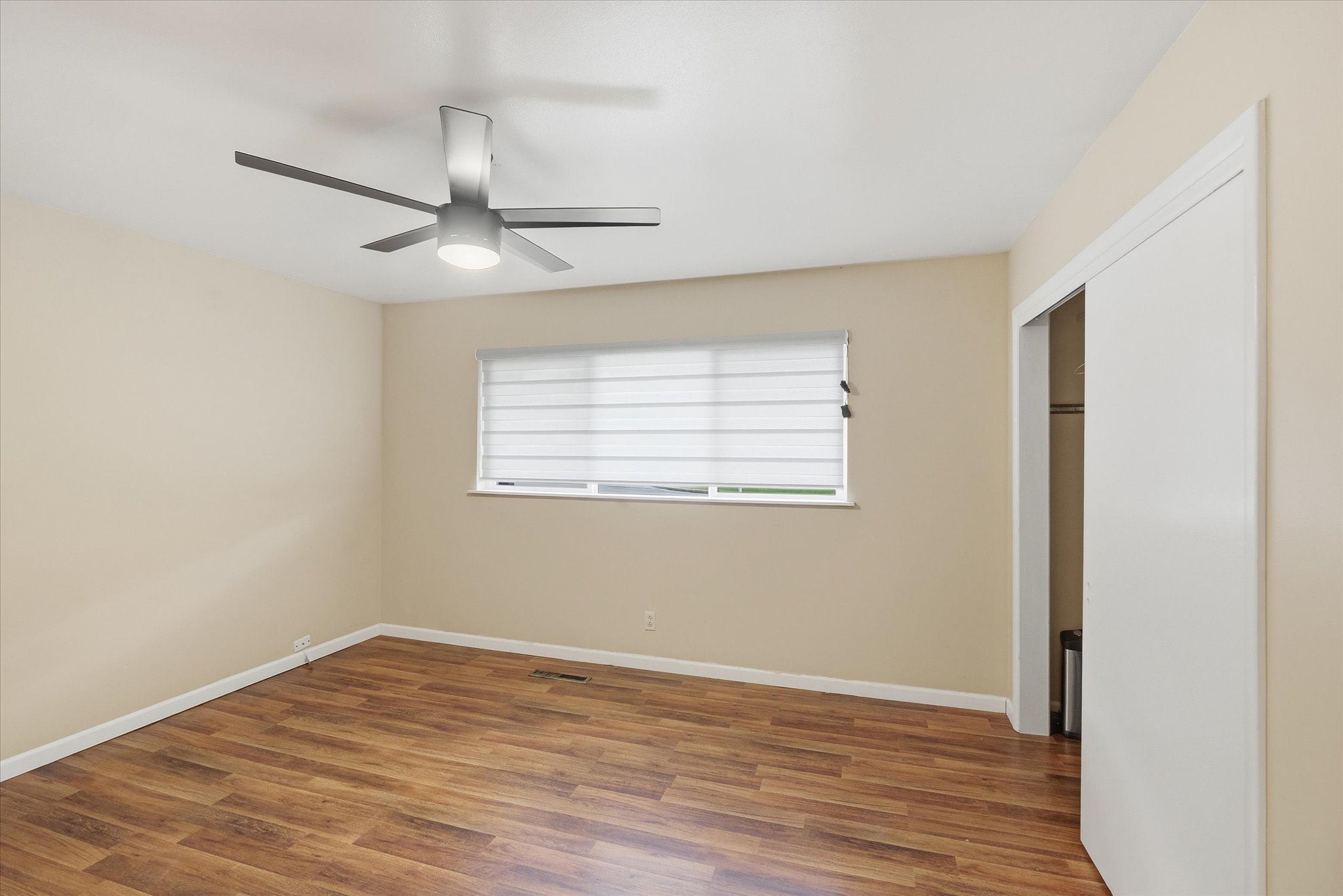 Spacious room featuring wood-finish flooring, a modern ceiling fan with integrated lighting, and a window with horizontal blinds